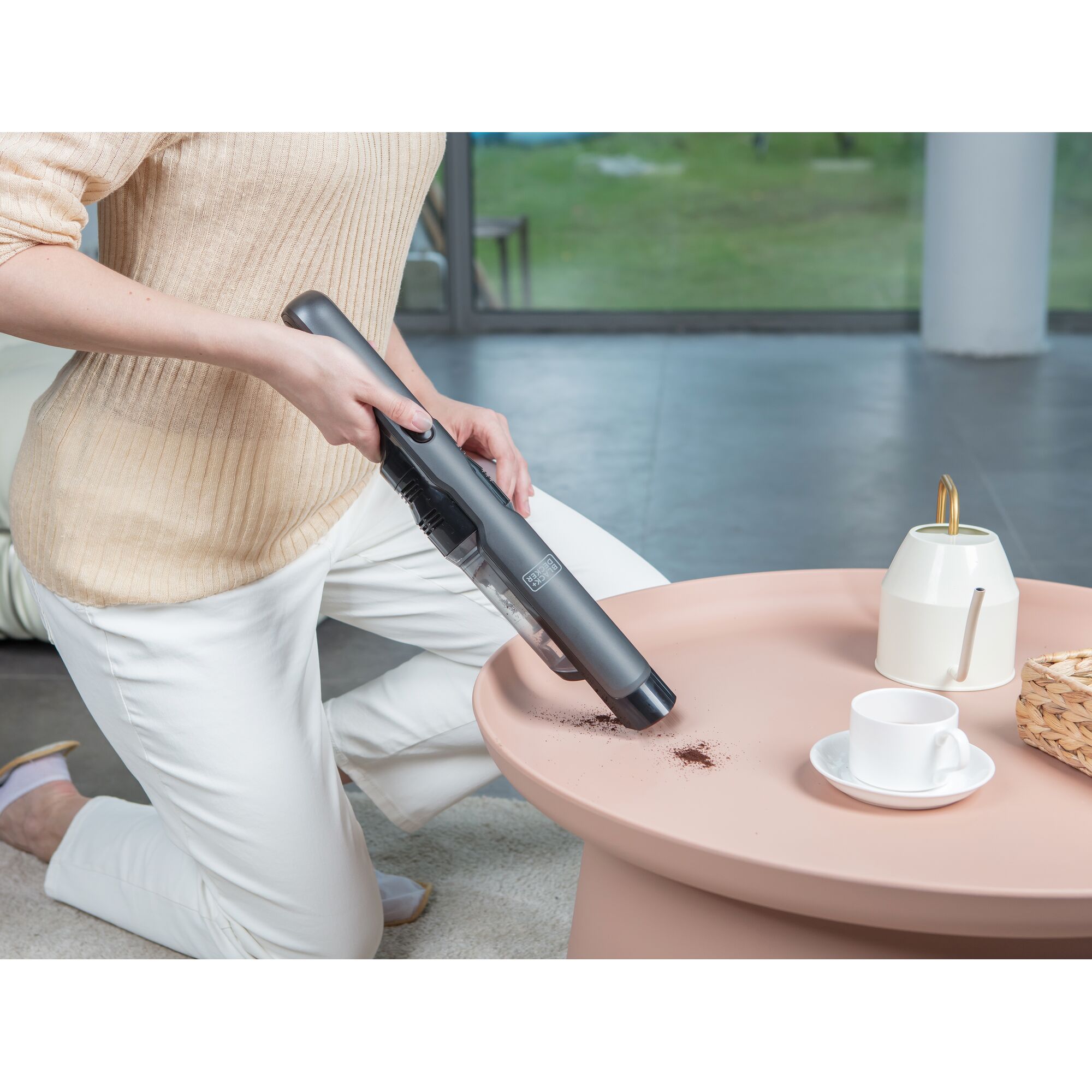 BLACKDECKER DVC320B01 handheld vacuum cleaning coffee grounds on pink table, cup and pot visible.
