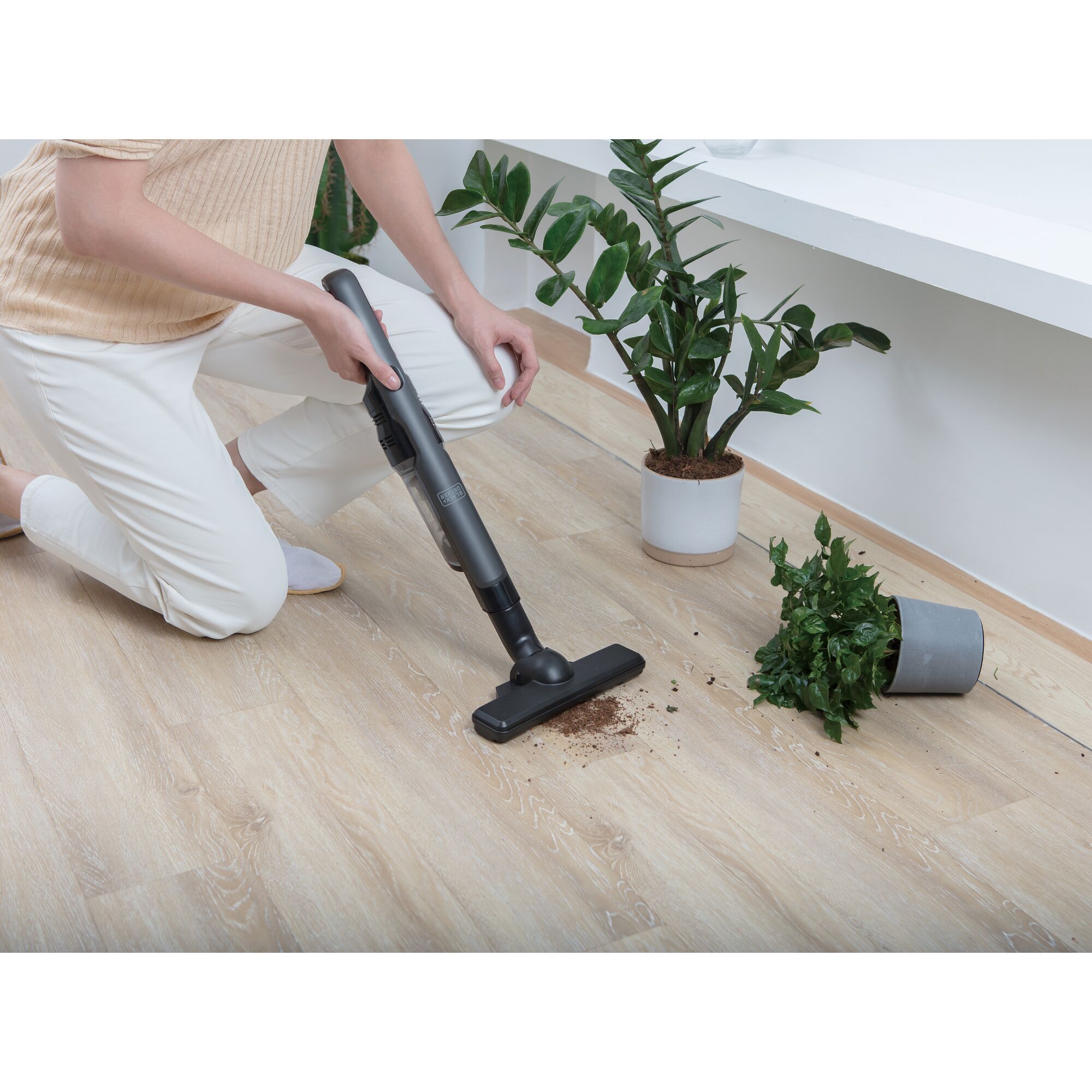 BLACKDECKER DVC320B01 stick vacuum cleaning spilled soil near tipped plant on light wood floor.