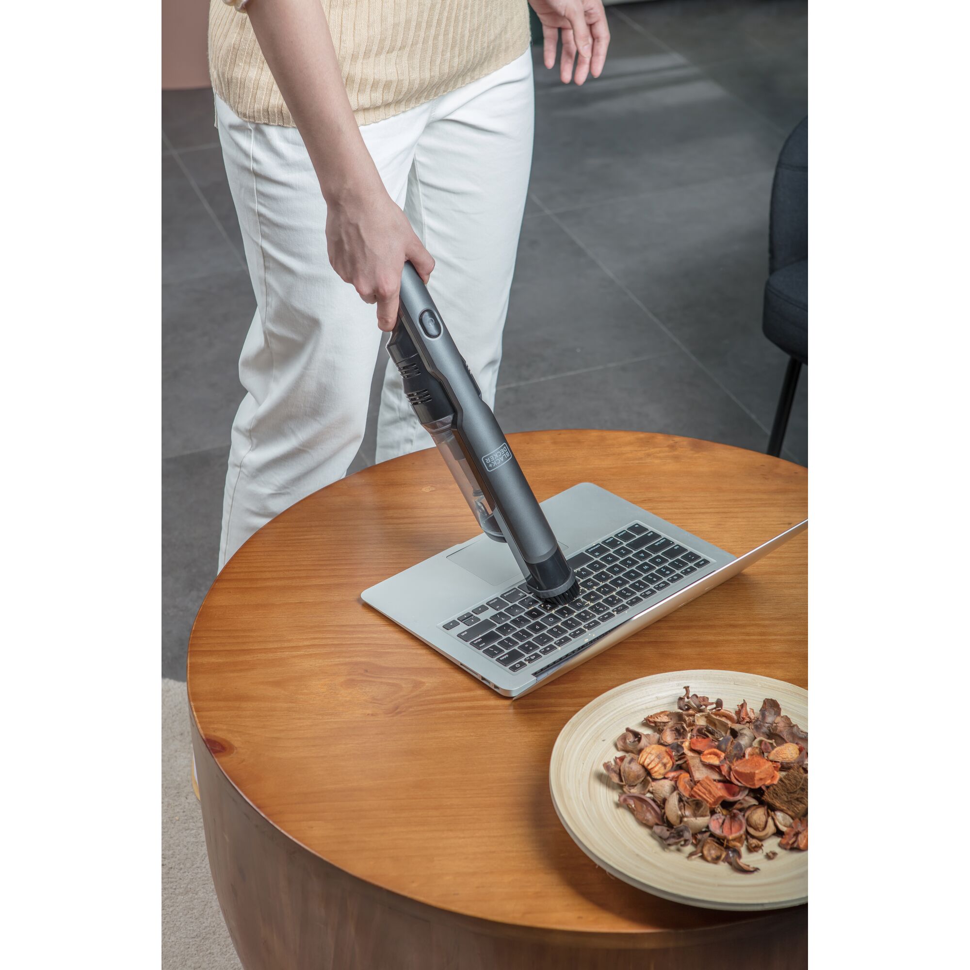 BLACKDECKER DVC320B01 handheld vacuum cleaning laptop keyboard on wooden table near bowl of potpourri.