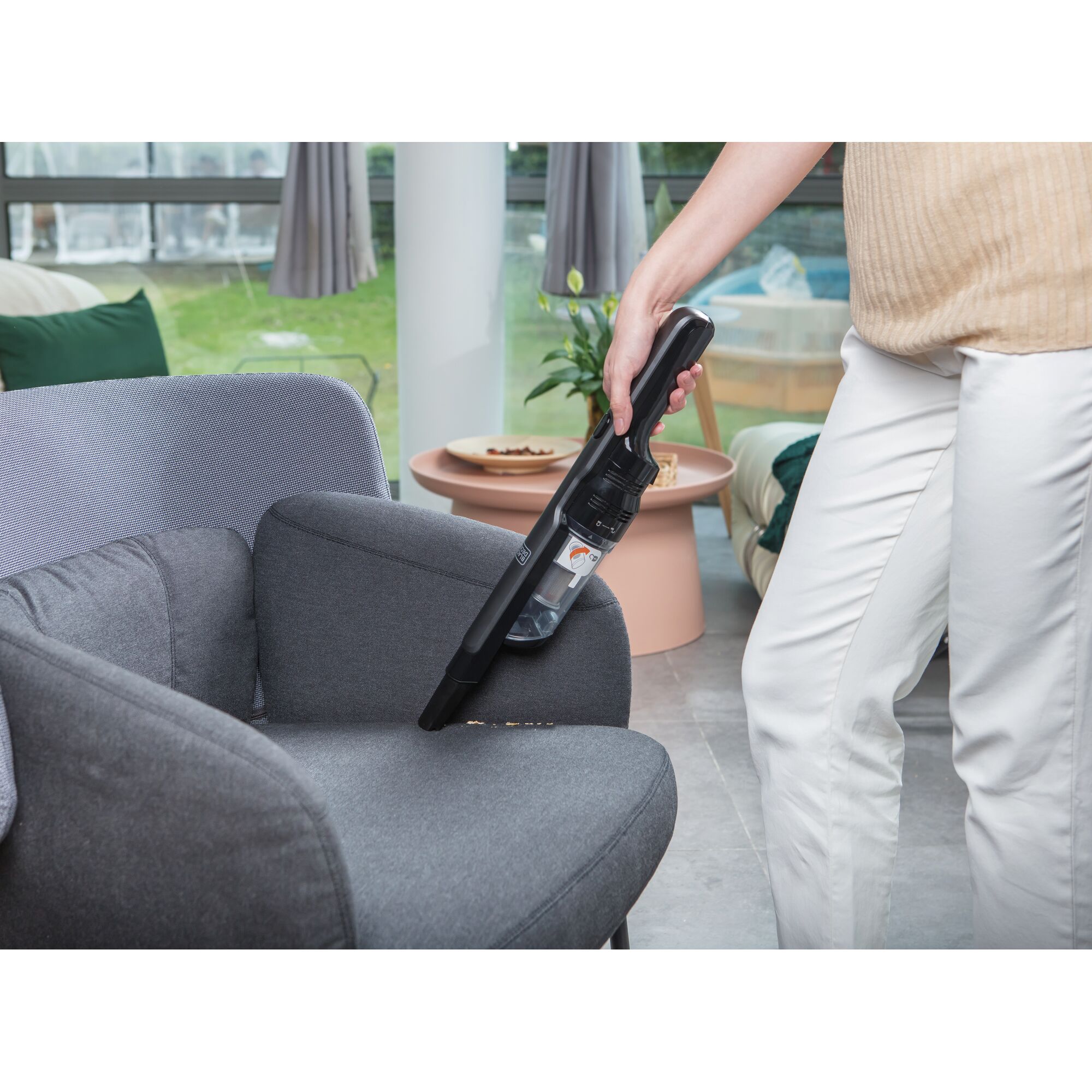 BLACKDECKER DVC320B01 handheld vacuum cleaning a gray armchair in a modern living room.