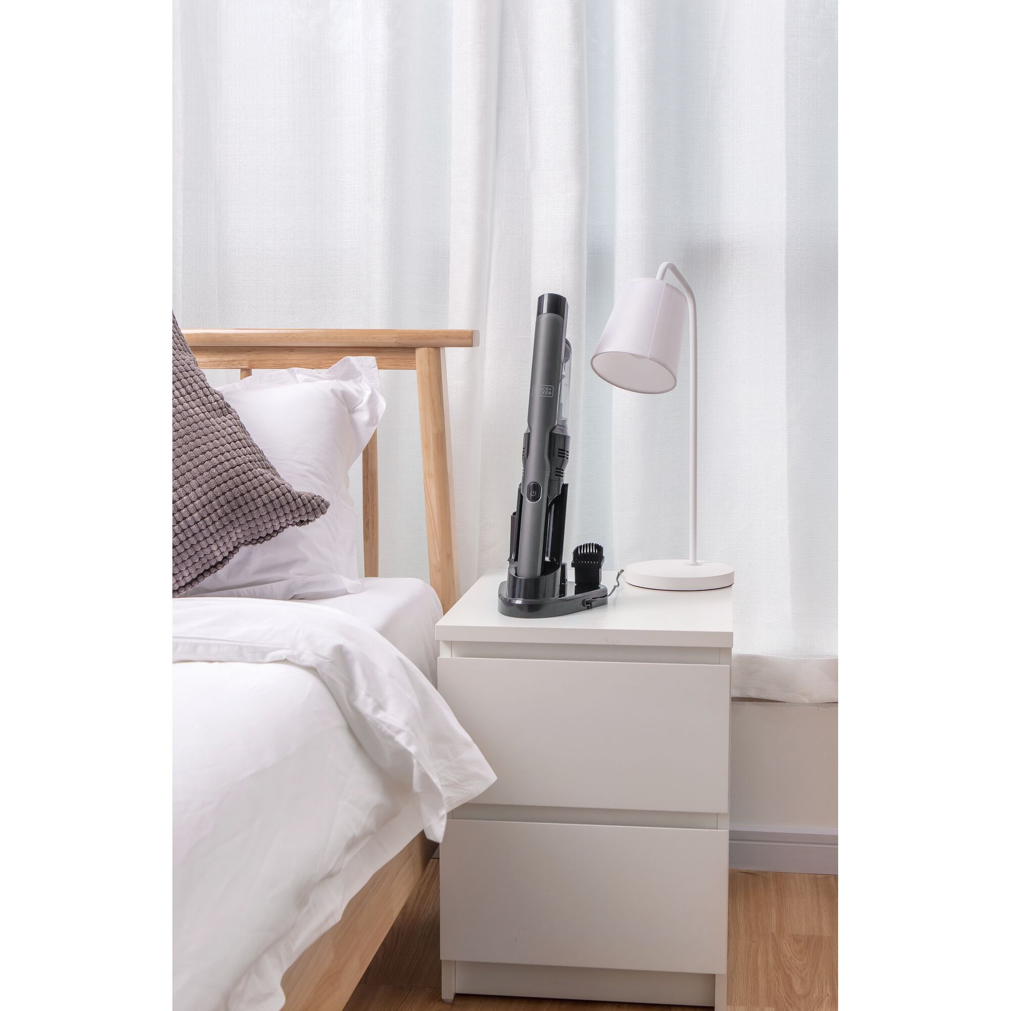 BLACKDECKER DVC320B01 handheld vacuum on white nightstand beside bed and lamp in bedroom setting.