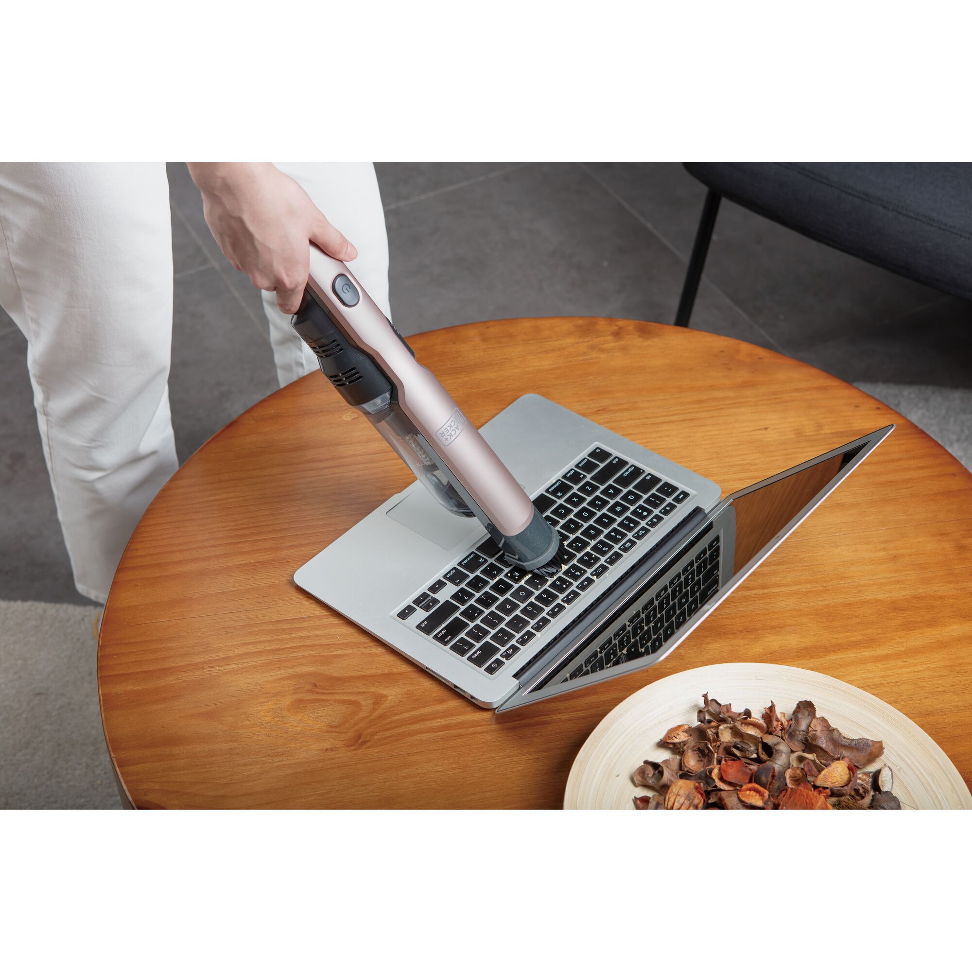 BLACKDECKER DVC320B24 handheld vacuum cleaning laptop keyboard on wood table, angled view.