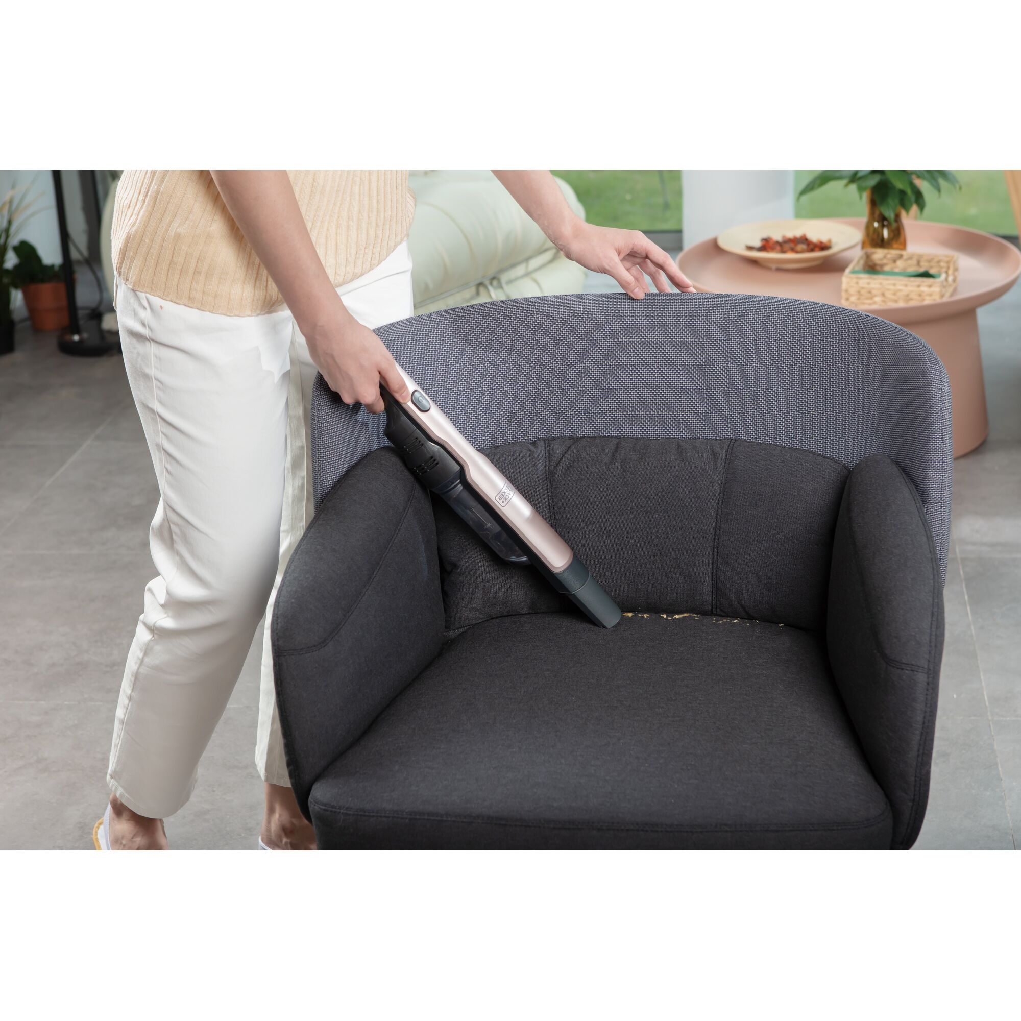 BLACKDECKER DVC320B24 handheld vacuum cleaner used to clean a dark armchair in a modern living room.