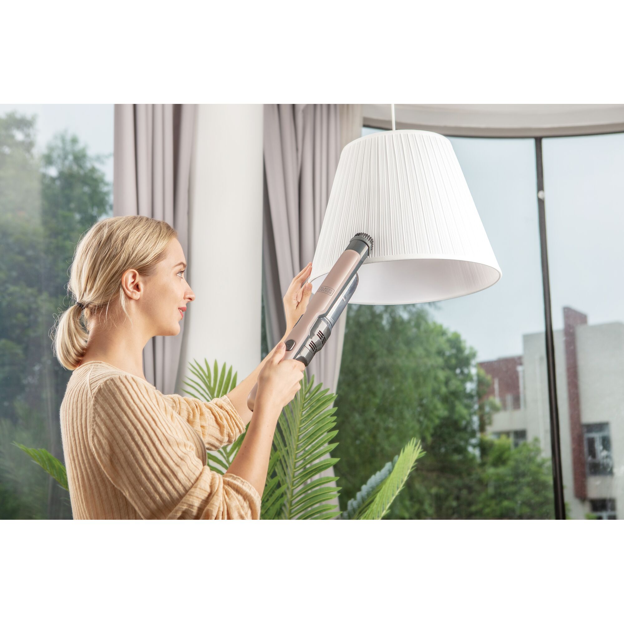BLACKDECKER DVC320B24 handheld vacuum used to clean a white lampshade indoors near a window.