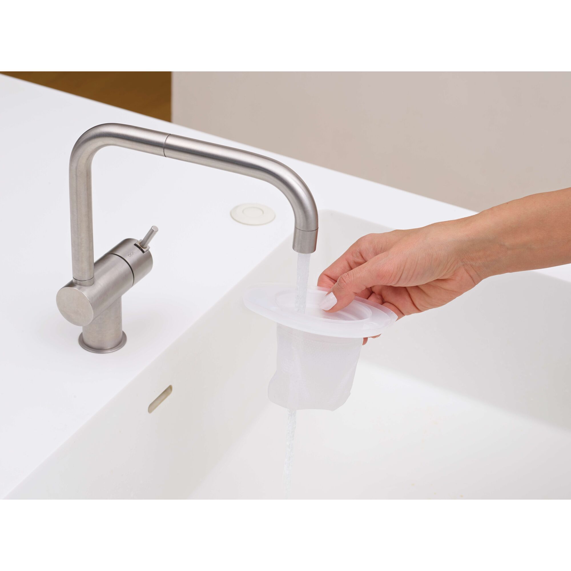 A hand rinsing a white mesh filter under running water at a modern kitchen sink.