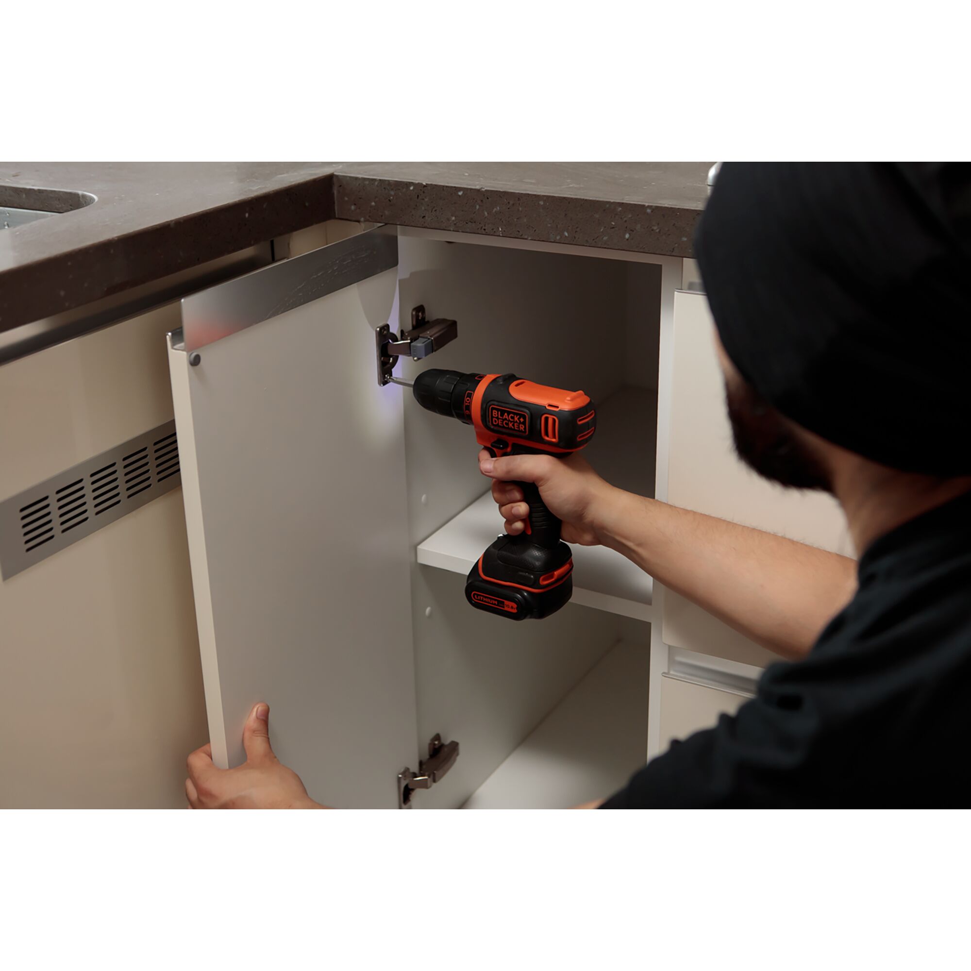 Person using BLACKDECKER EBDCDD12HS cordless drill to install hinge in white kitchen cabinet.