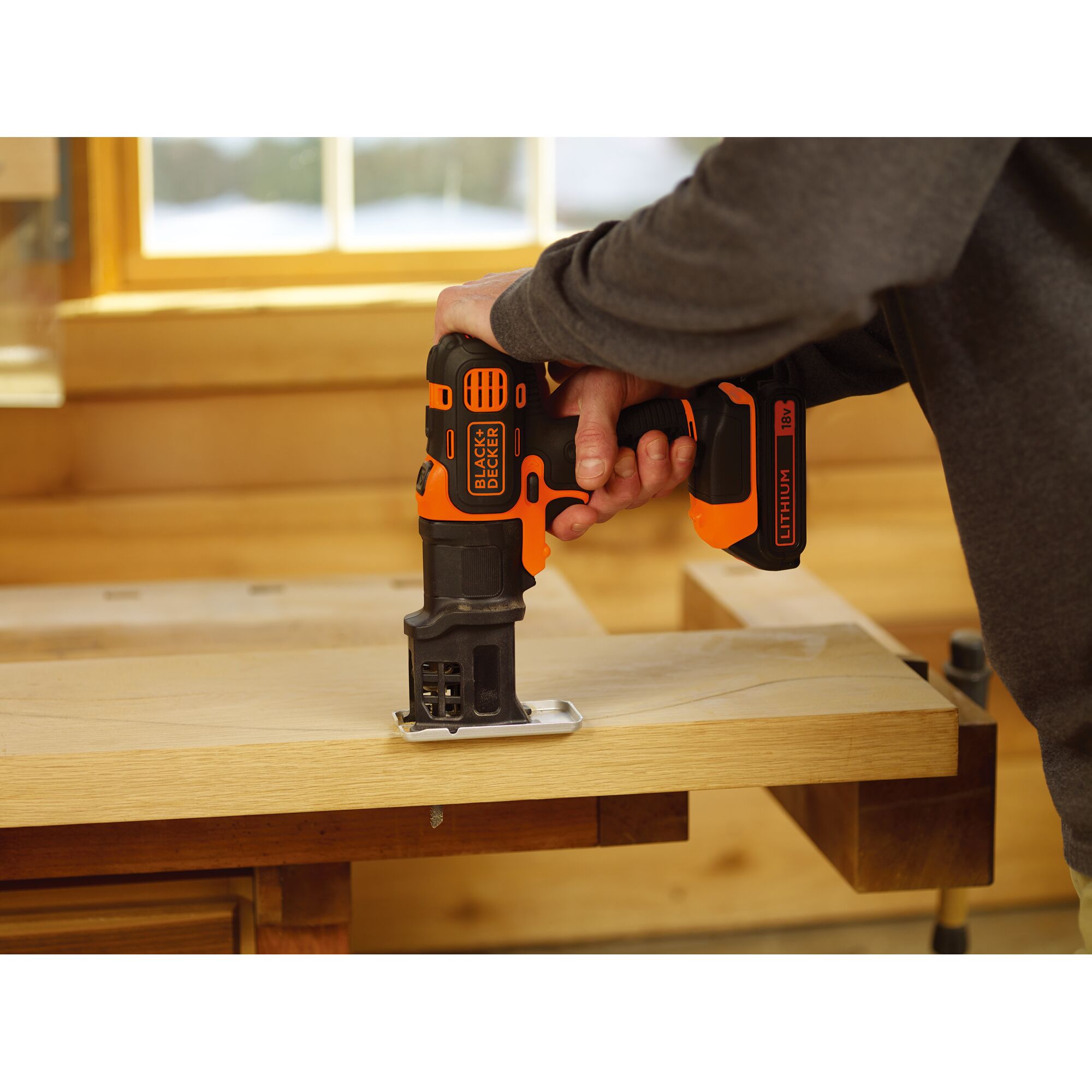 BLACKDECKER EJS183 cordless jigsaw in use cutting wood, black and orange, woodworking setting.