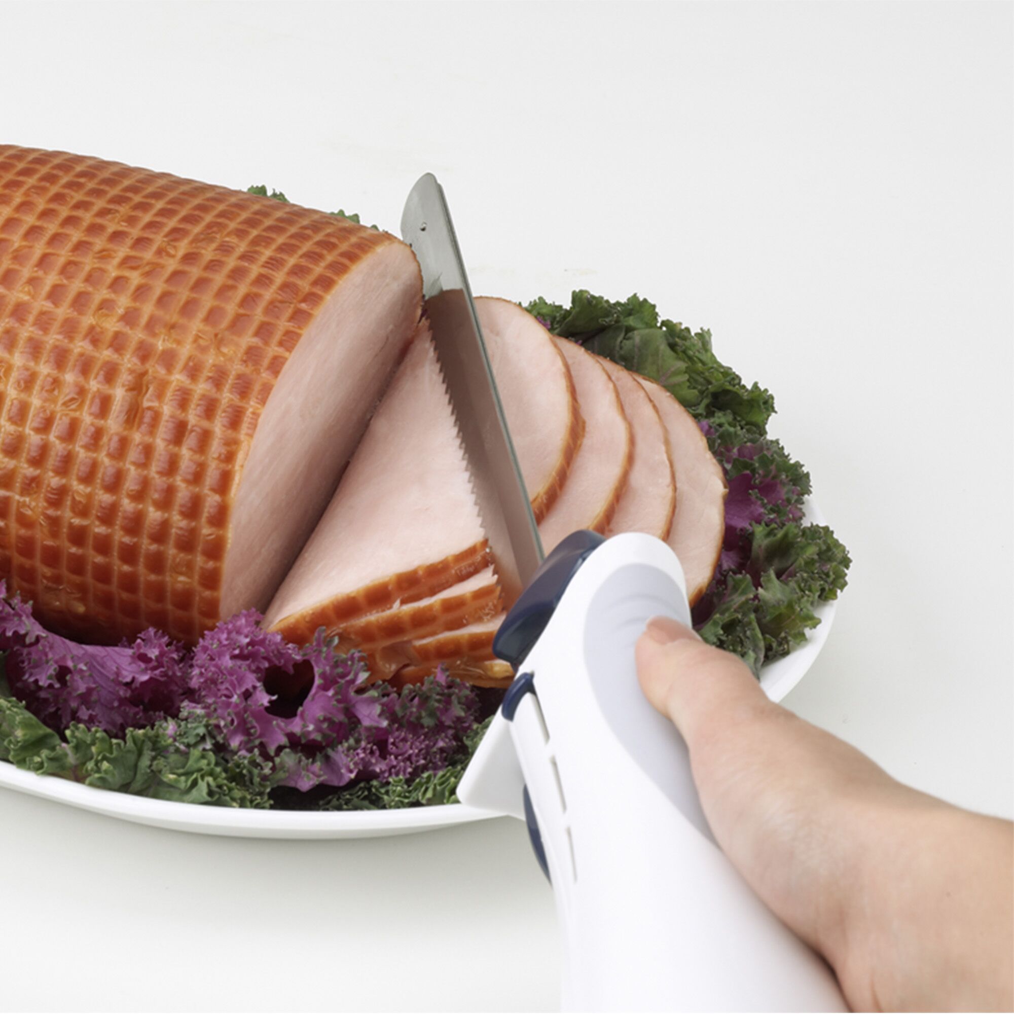 BLACKDECKER EK700 electric knife slicing ham on white plate with greens, close up side angle.