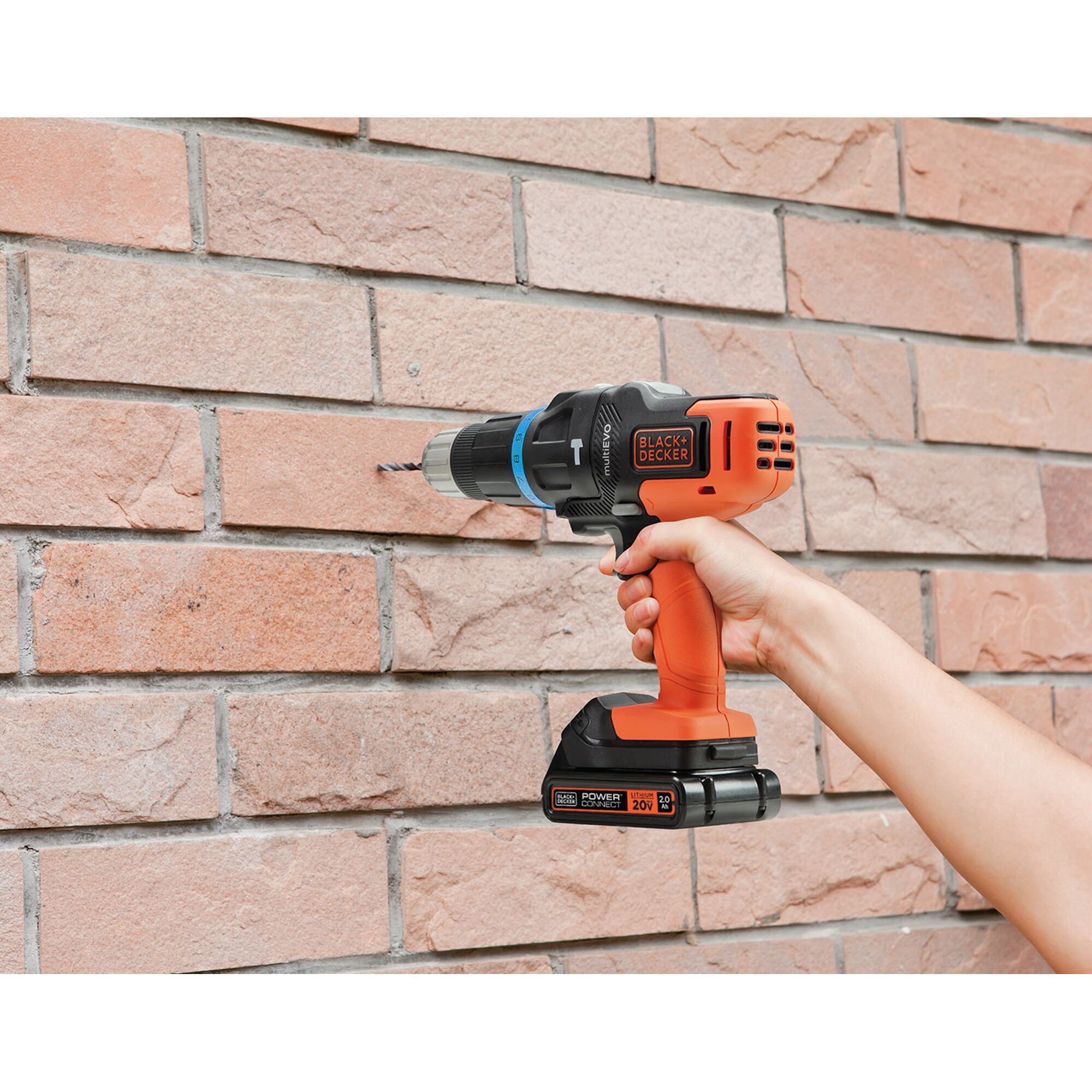 Photo of BLACK+DECKER EVO185H1 cordless drill in use drilling brick wall, orange and black with 20V battery.