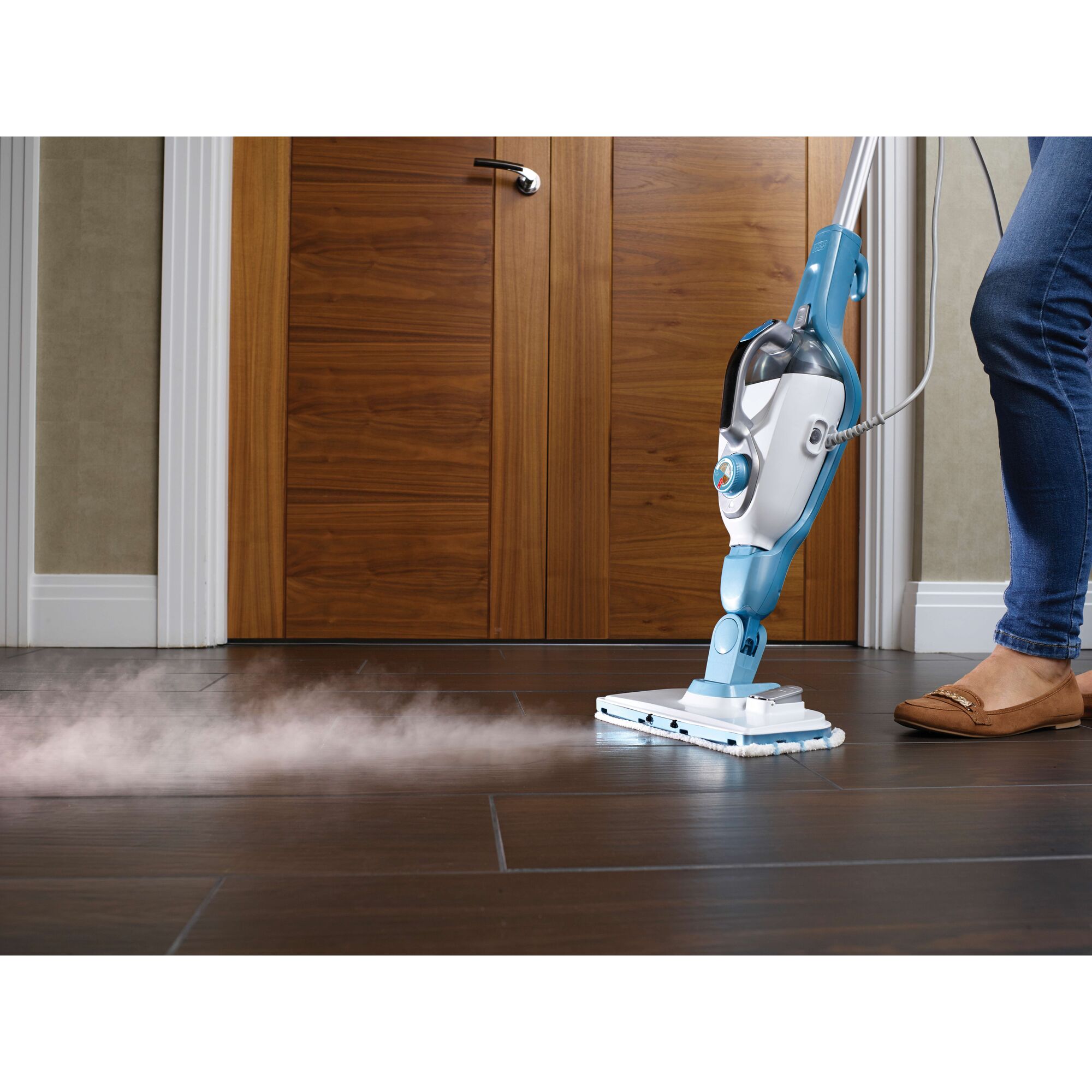 A person using a BLUE and white BLACK+DECKER steam mop to clean a dark tiled floor. Steam is visibly coming out from the mop head.