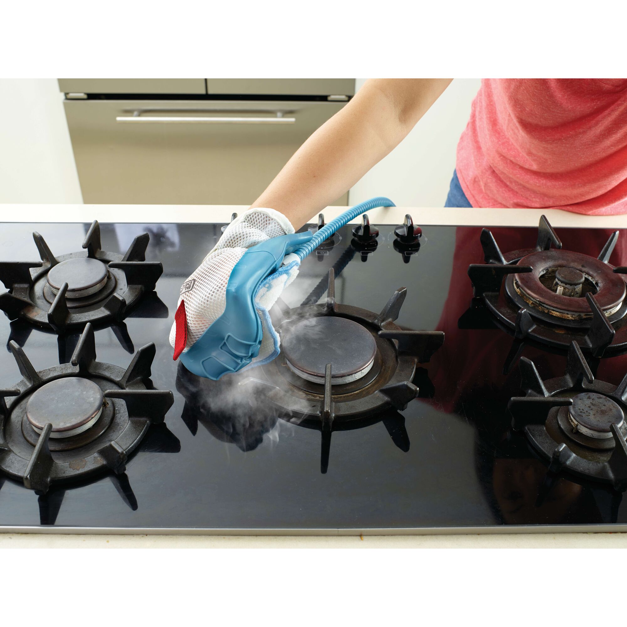 A person is using a steam cleaning glove to clean a gas stove top, producing visible steam.