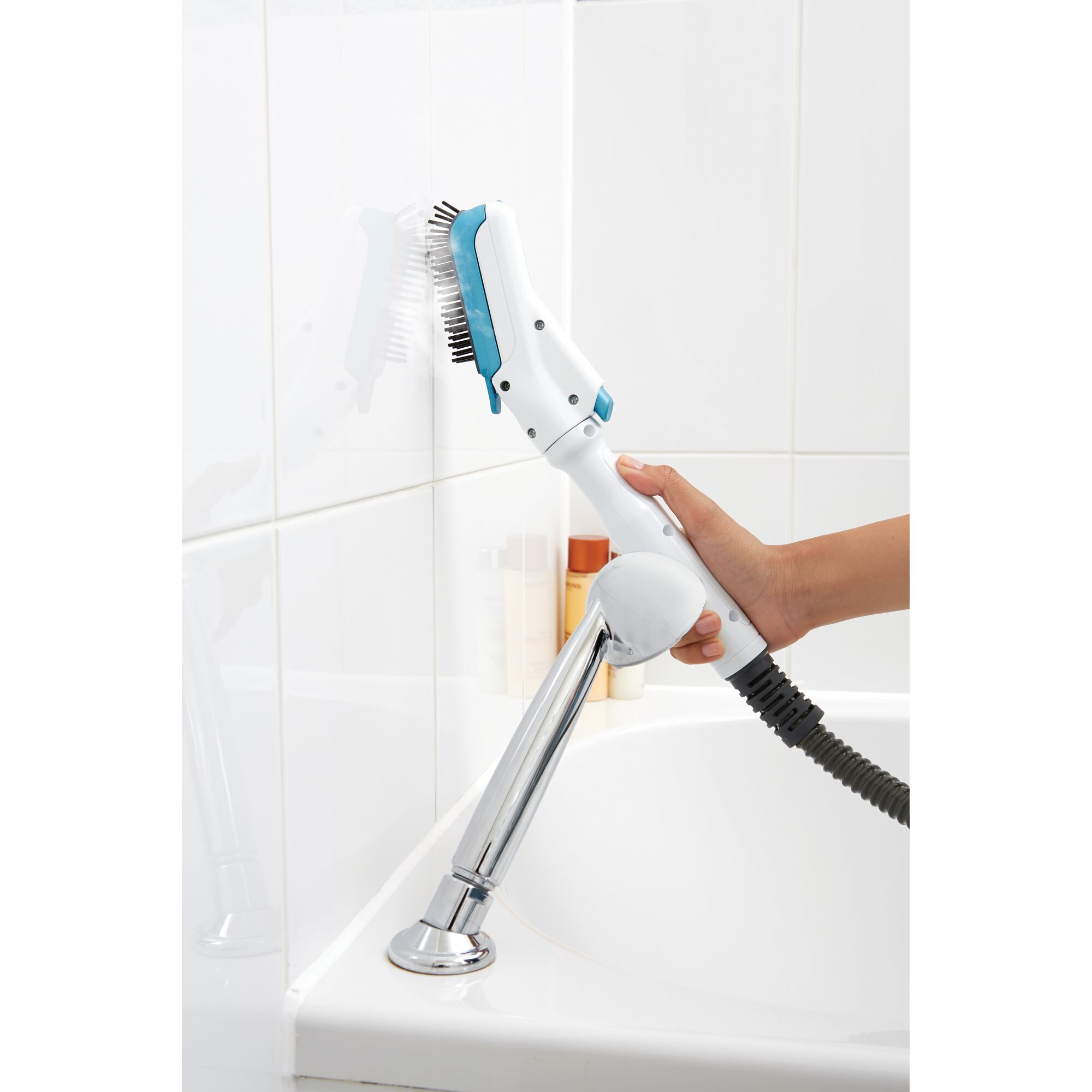 A hand using a BLACK+DECKER steam cleaning brush to clean white bathroom tiles next to a bathtub.