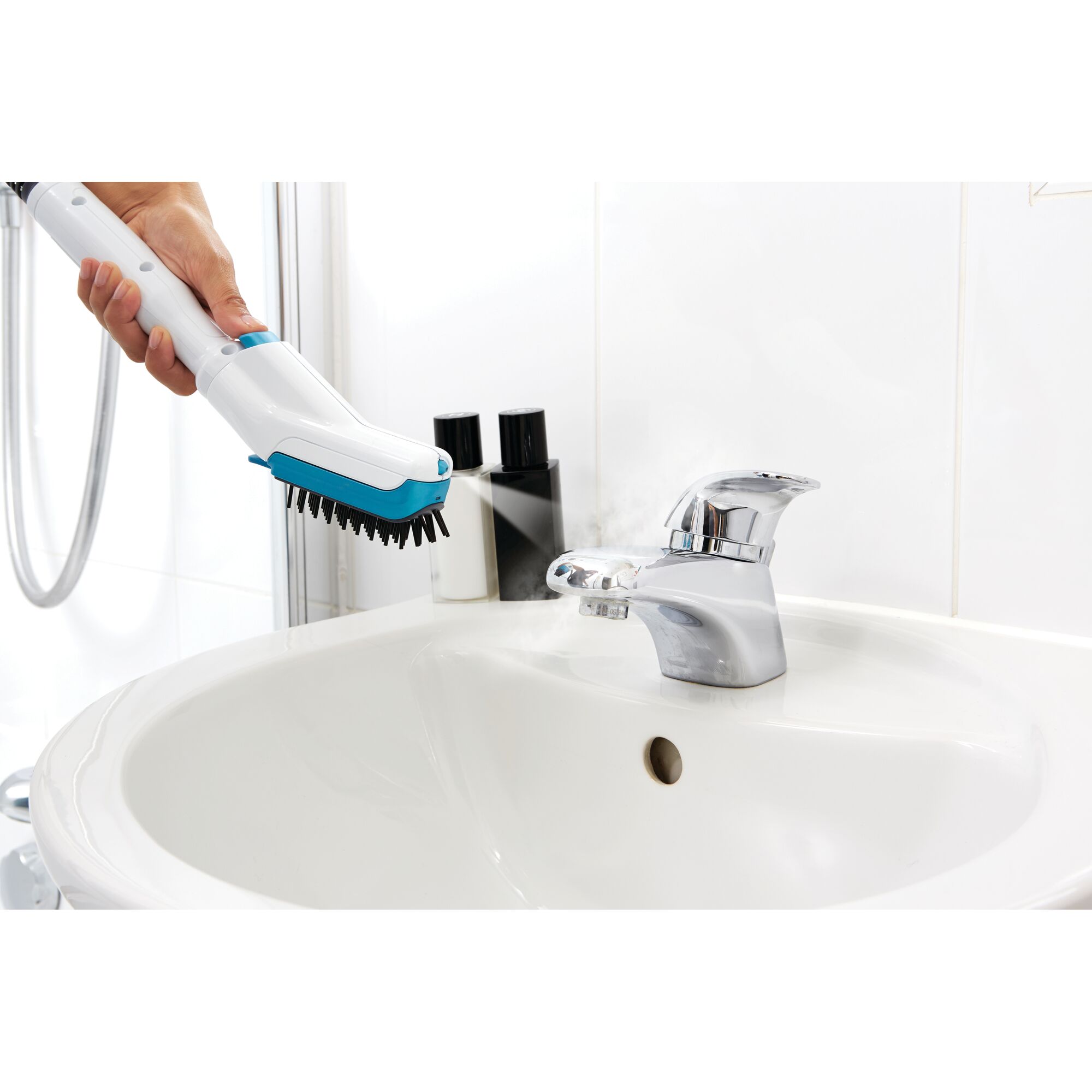 A person using a BLACK+DECKER steam cleaning brush to clean a bathroom sink faucet. The brush emits steam while cleaning the shiny chrome faucet.