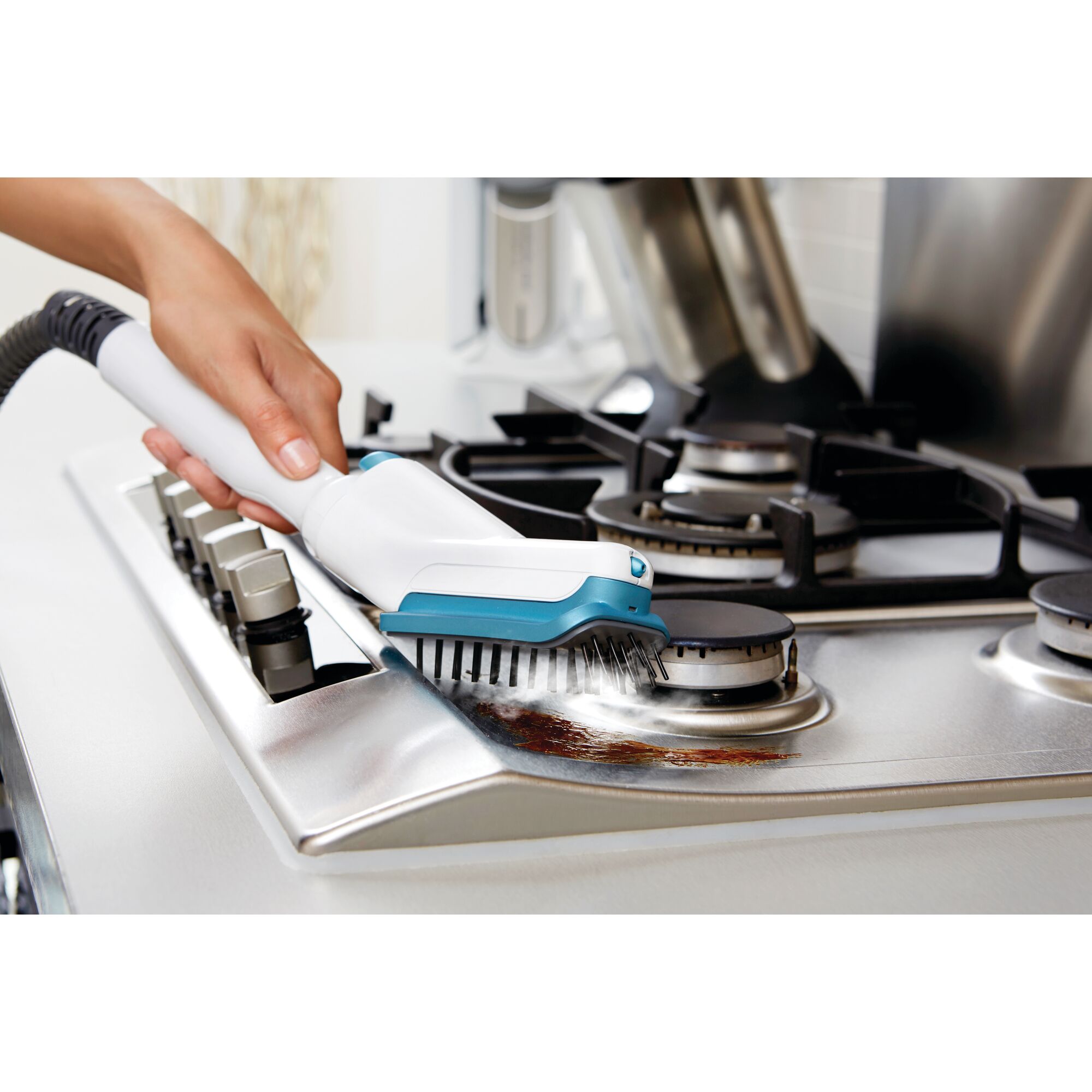 A person is using a BLACK+DECKER steam cleaning tool to clean a stainless steel gas stove, focusing on removing grime and stains around the burners.