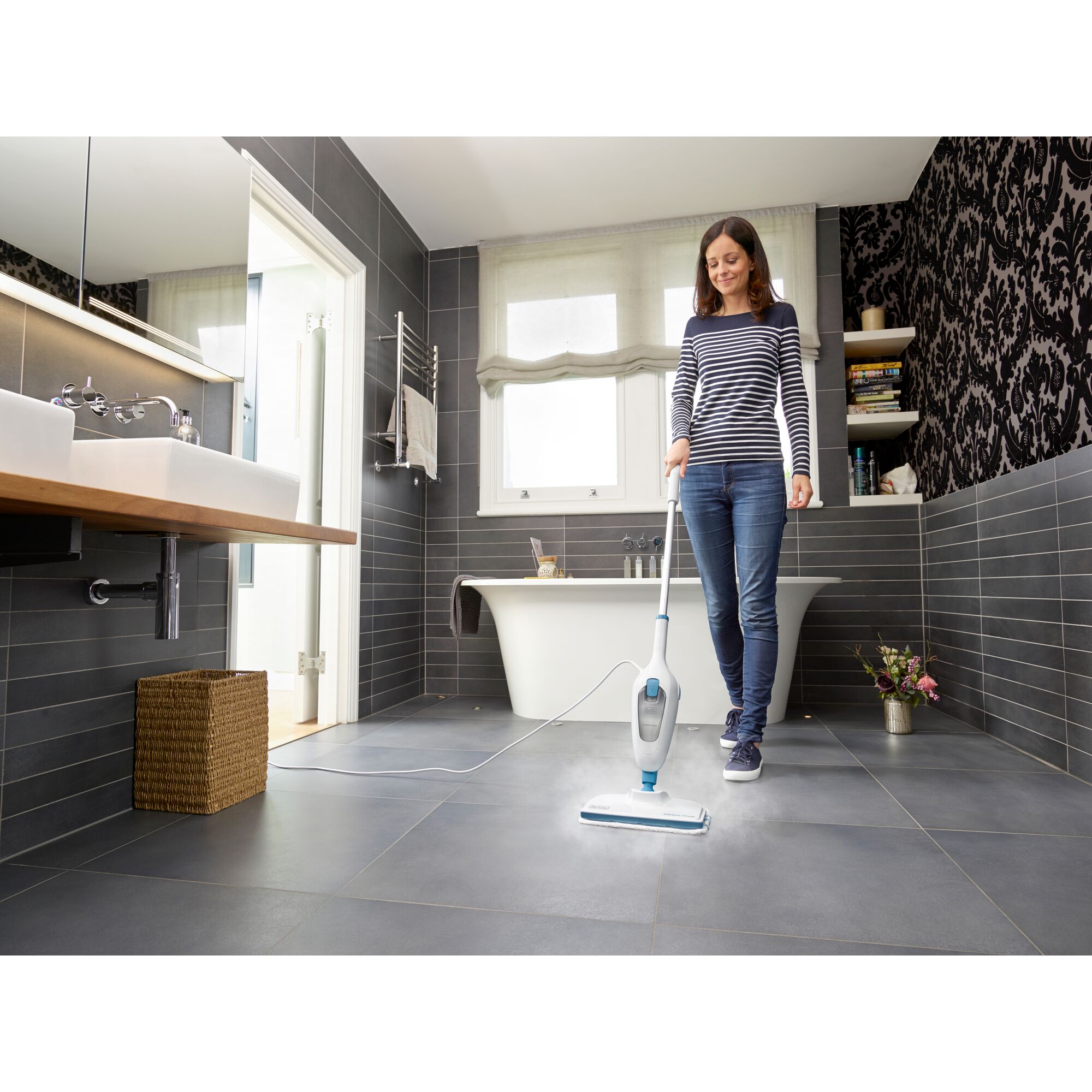 BLACKDECKER FSMH13E5 steam mop cleaning gray tile bathroom floor, held by person in striped shirt.