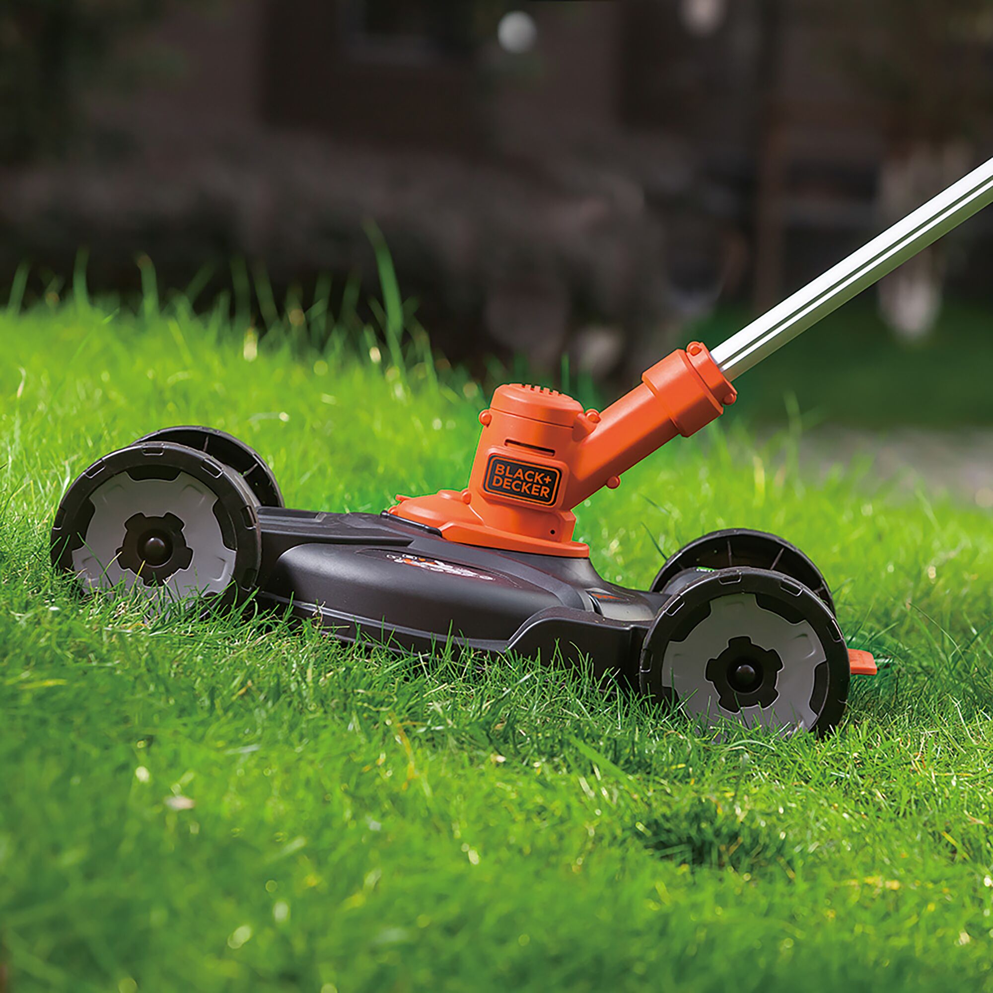 BLACKDECKER GCM18BN lawn mower with orange and black body, cutting grass outdoors.