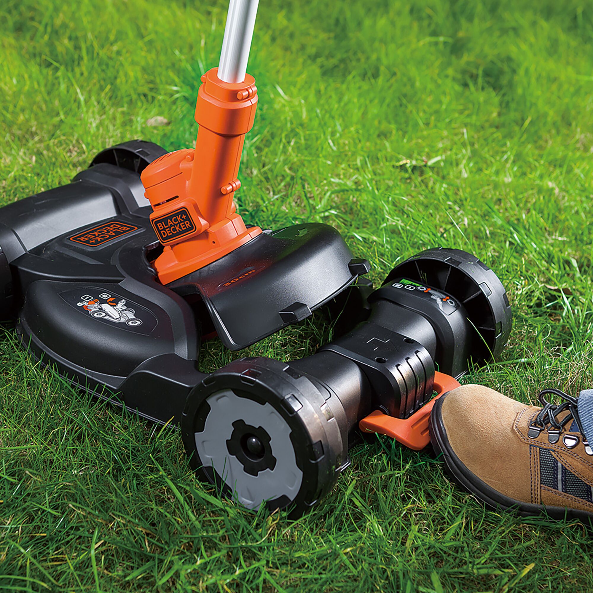 BLACKDECKER GCM18BN cordless lawn mower close-up on grass, showing wheels and orange handle.