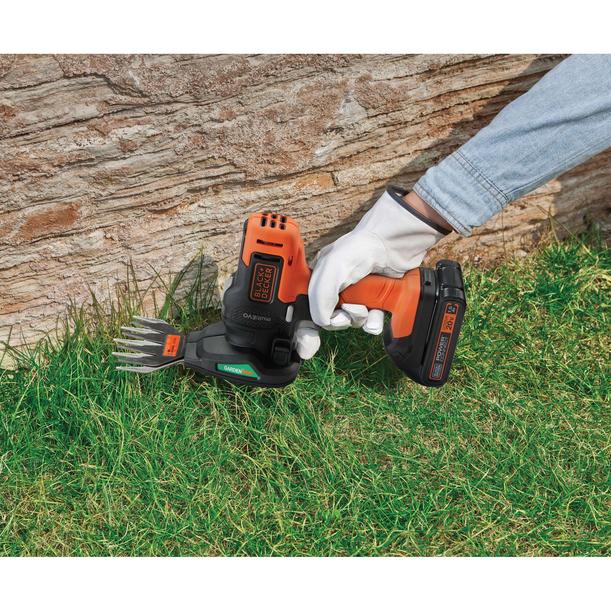 BLACKDECKER GEH183 hedge and grass trimmer handheld, orange and black, used on lawn near stone wall.