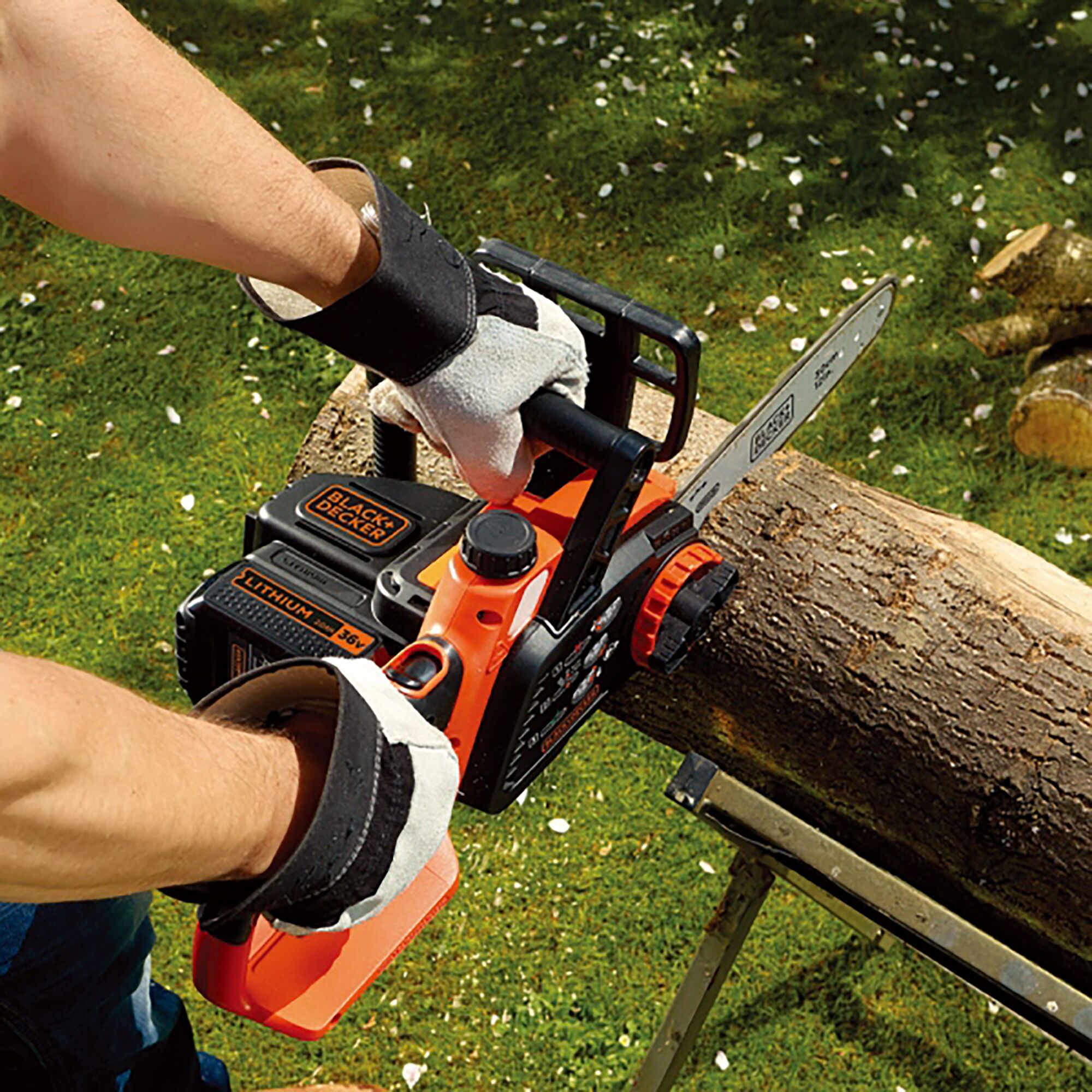 BLACKDECKER GKC3630L cordless chainsaw cutting log outdoors, visible lithium battery and safety gloves.