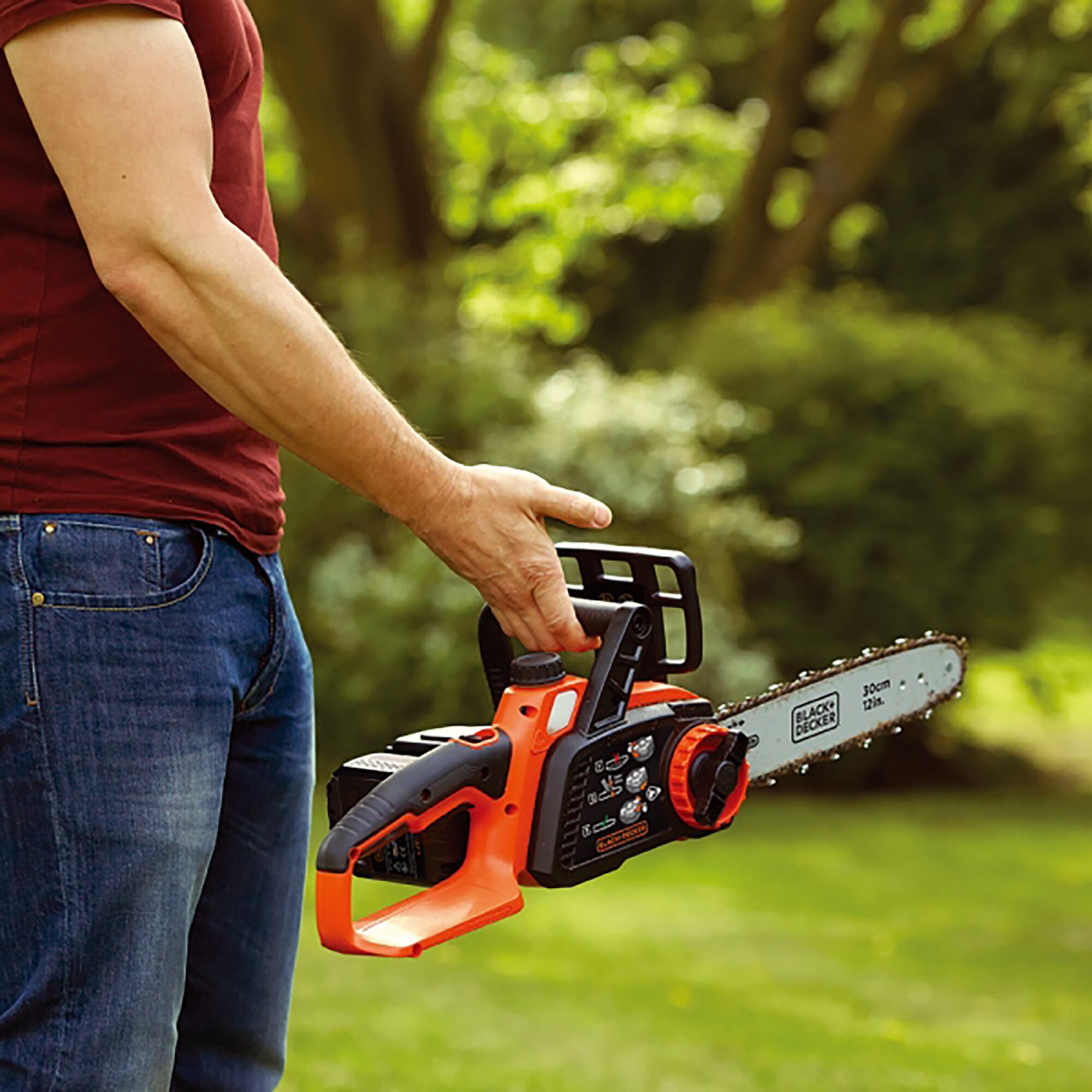Person holding BLACKDECKER GKC3630L cordless chainsaw outdoors, orange and black body, 30cm bar.