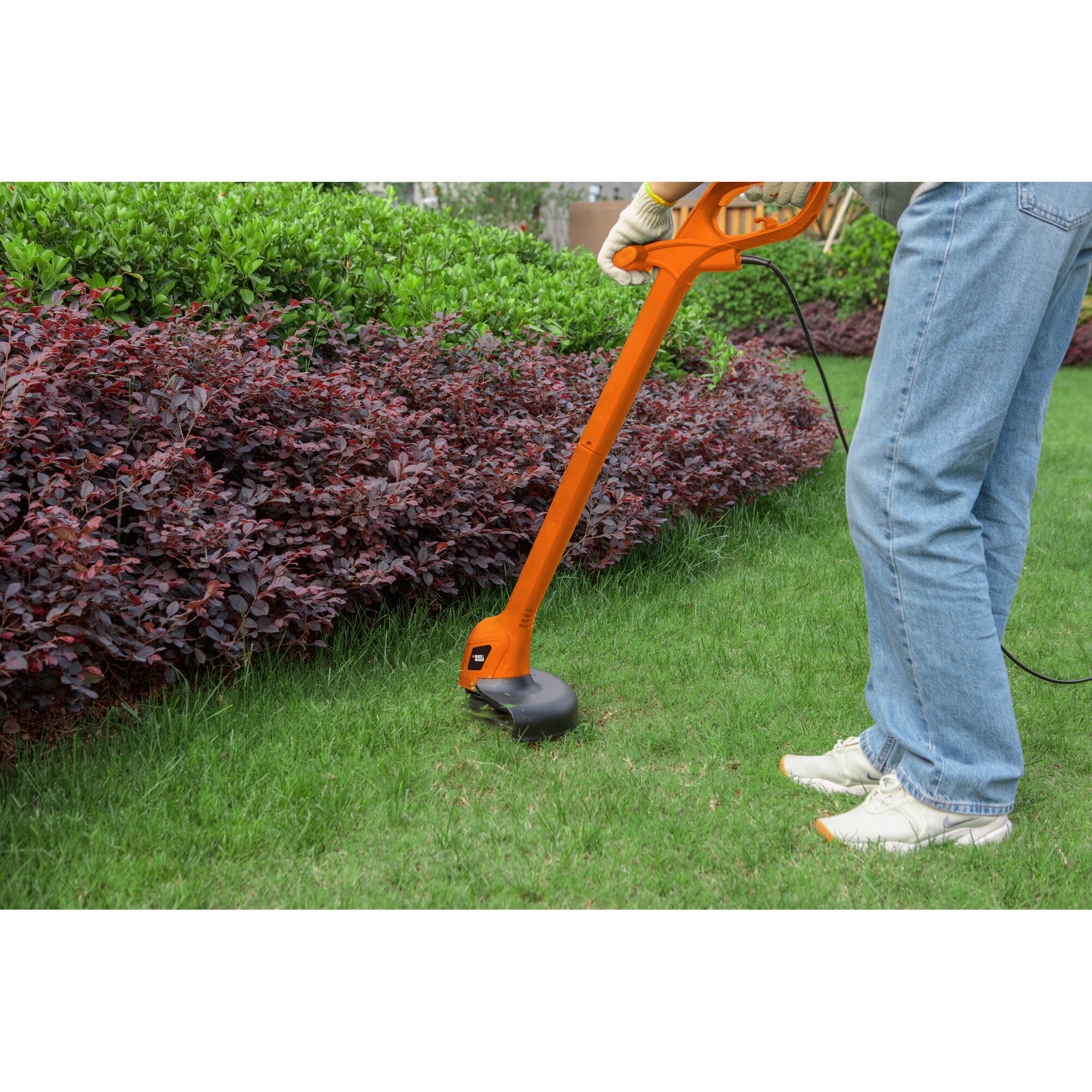 BLACKDECKER GL260 grass trimmer in use trimming lawn edges near bushes outdoors.