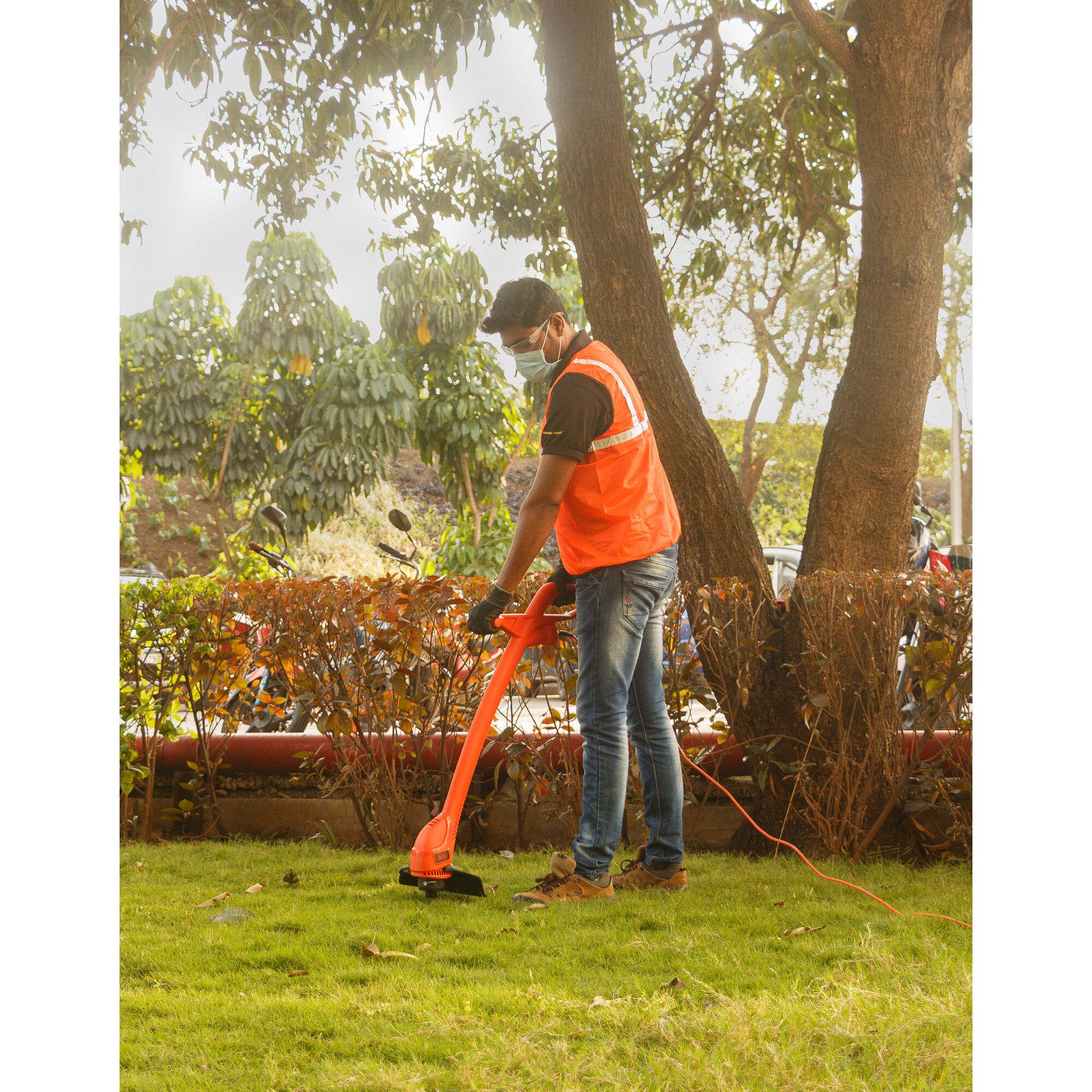 BLACKDECKER GL360 orange grass trimmer in use outdoors by worker in safety vest on lawn.