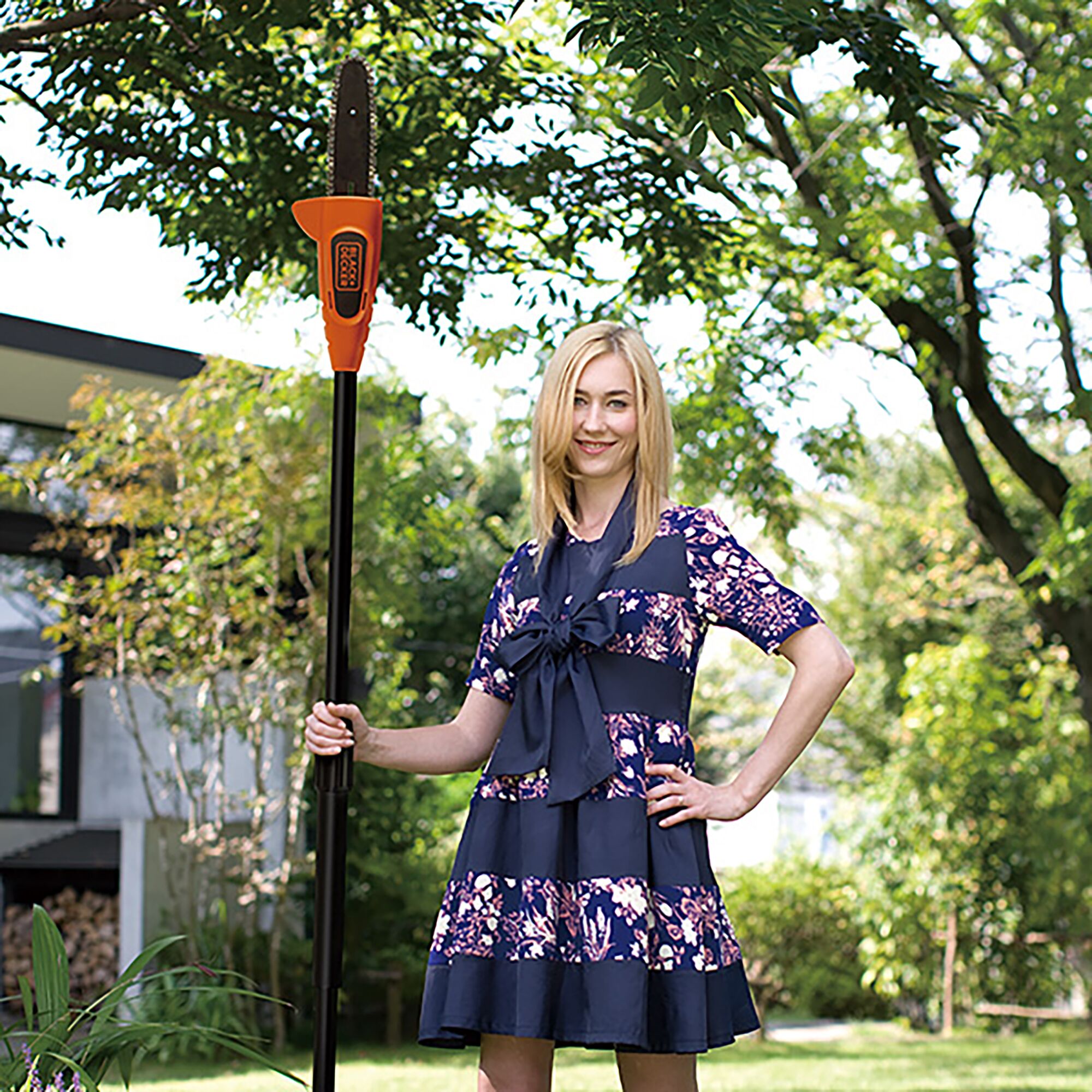 BLACKDECKER GPC1820LBN pole saw held vertically by a person outdoors in a green garden.