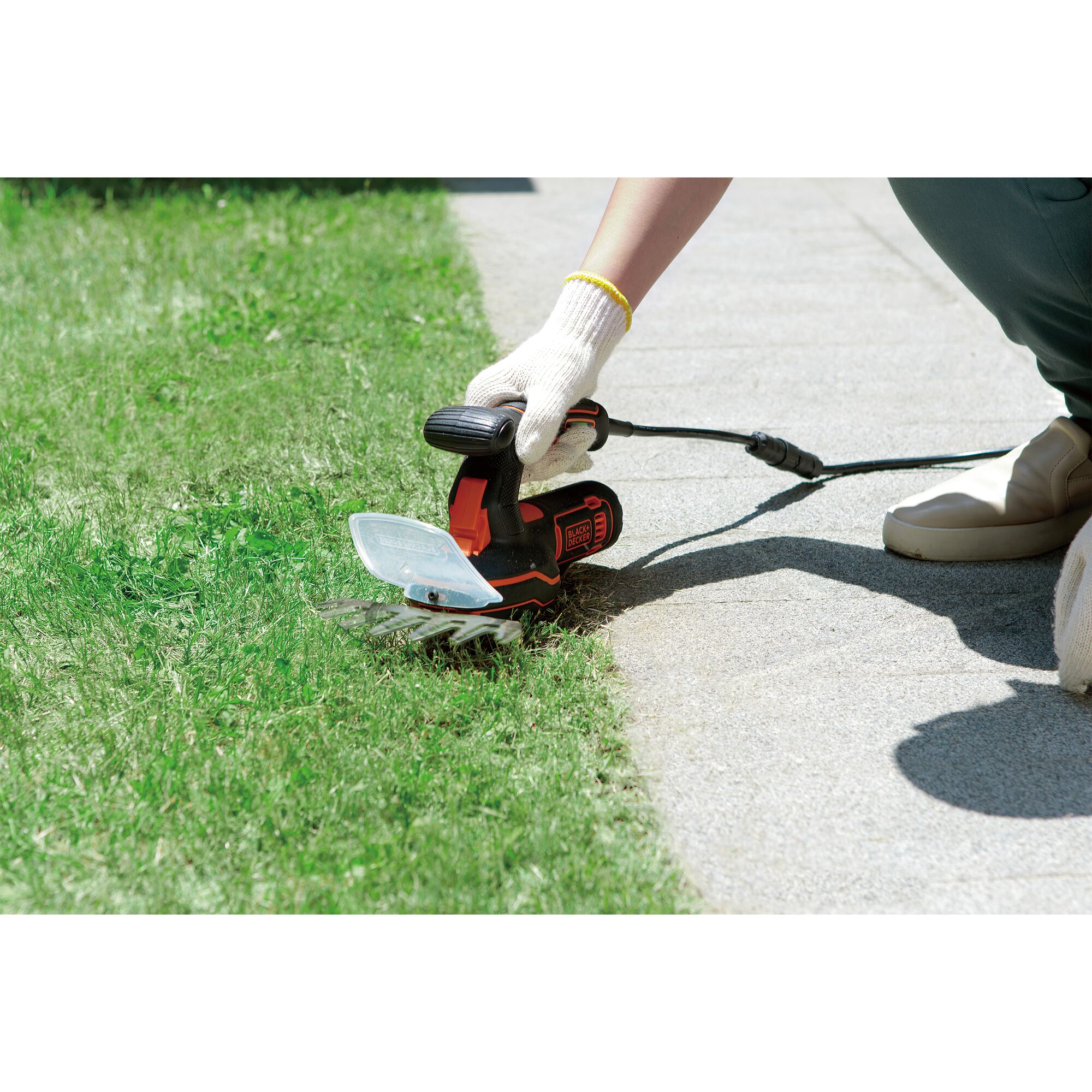 Photo of BLACKDECKER GPSH1820 handheld grass shear trimming lawn edge near sidewalk.