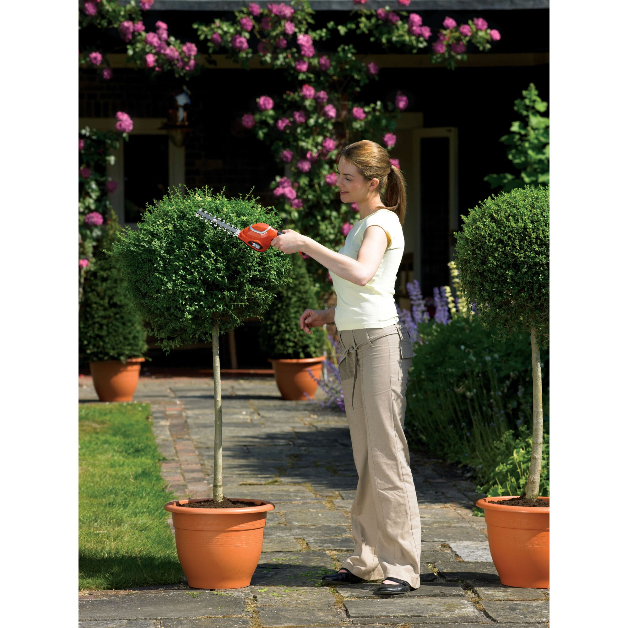 BLACKDECKER GSL700 cordless shrub trimmer used to shape potted bushes in a garden.