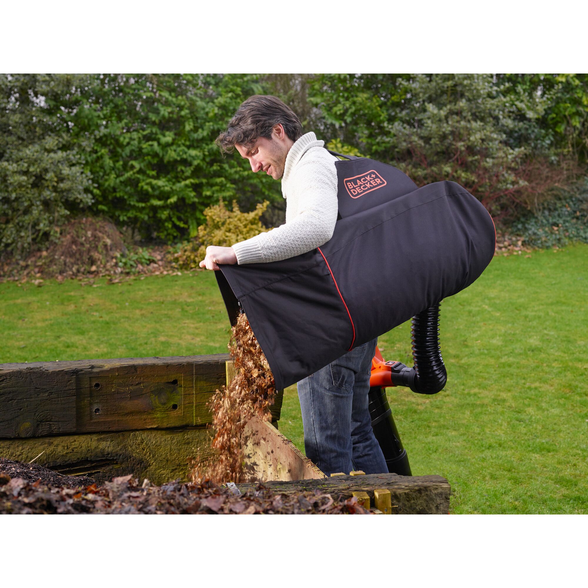 Photo of BLACKDECKER GW3031BP leaf collection bag in use, emptying leaves outdoors near a garden bed.