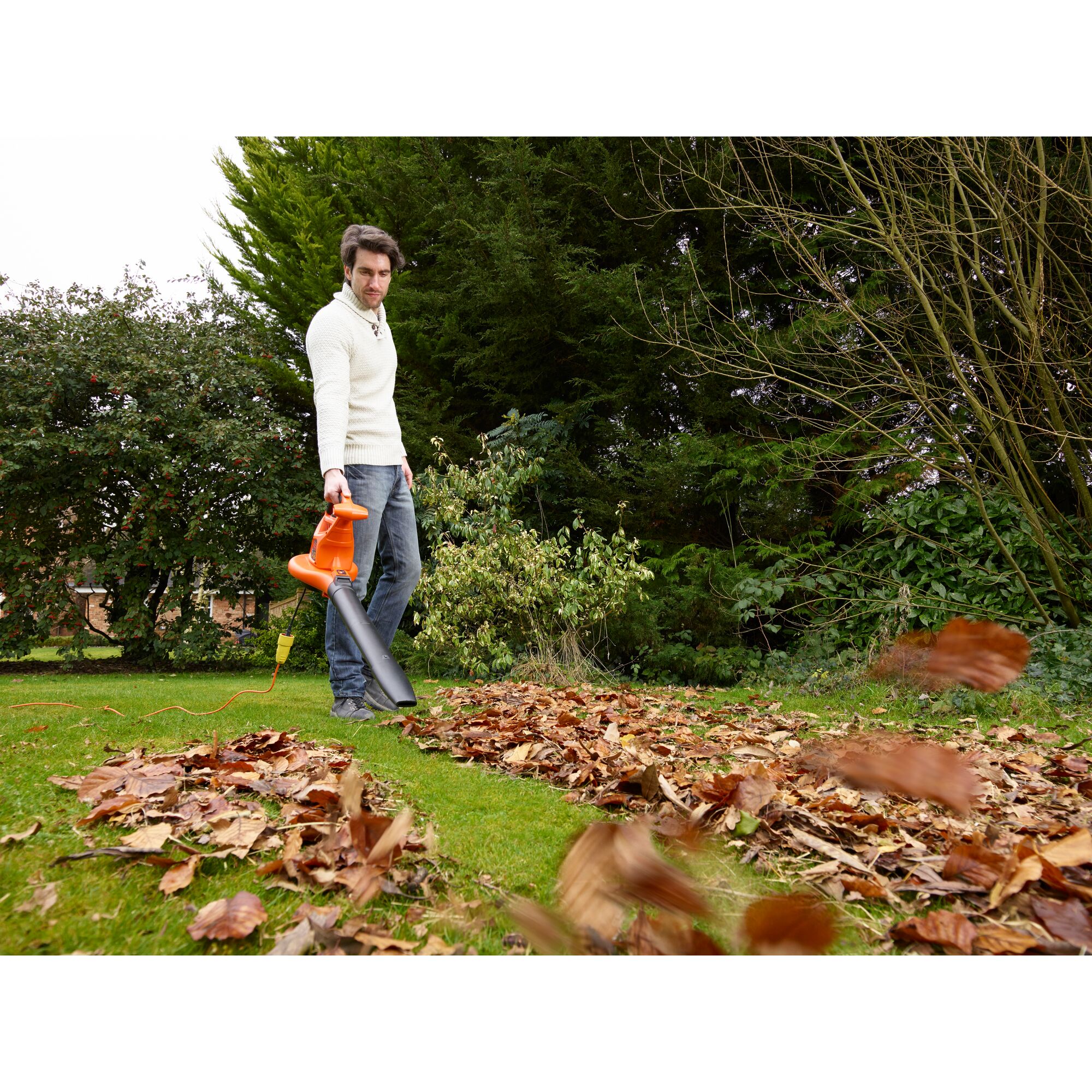 BLACKDECKER GW3031BP corded leaf blower in use outdoors clearing fallen leaves on grass.