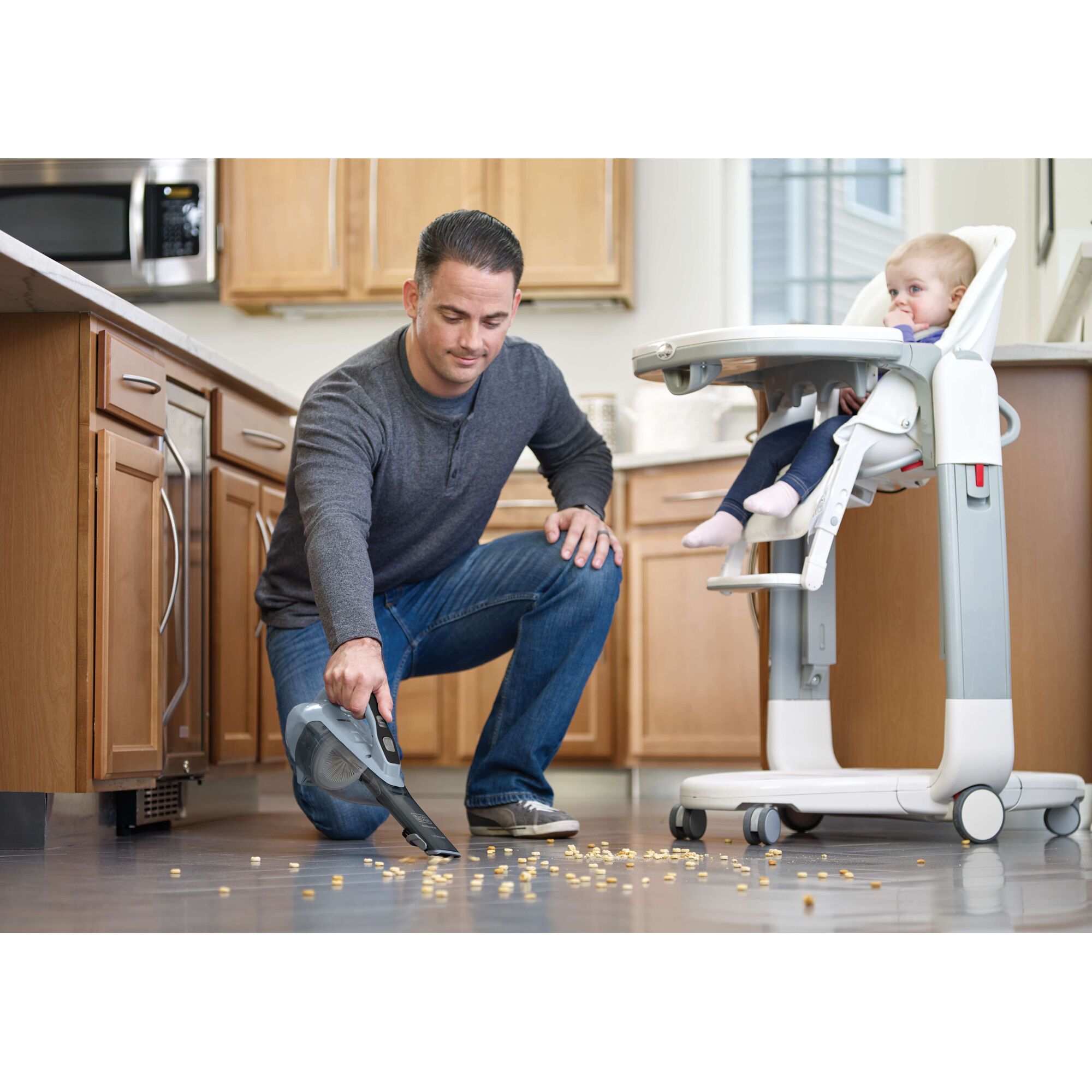 BLACKDECKER HLVA315J32 handheld vacuum cleaning spilled cereal in kitchen near high chair.