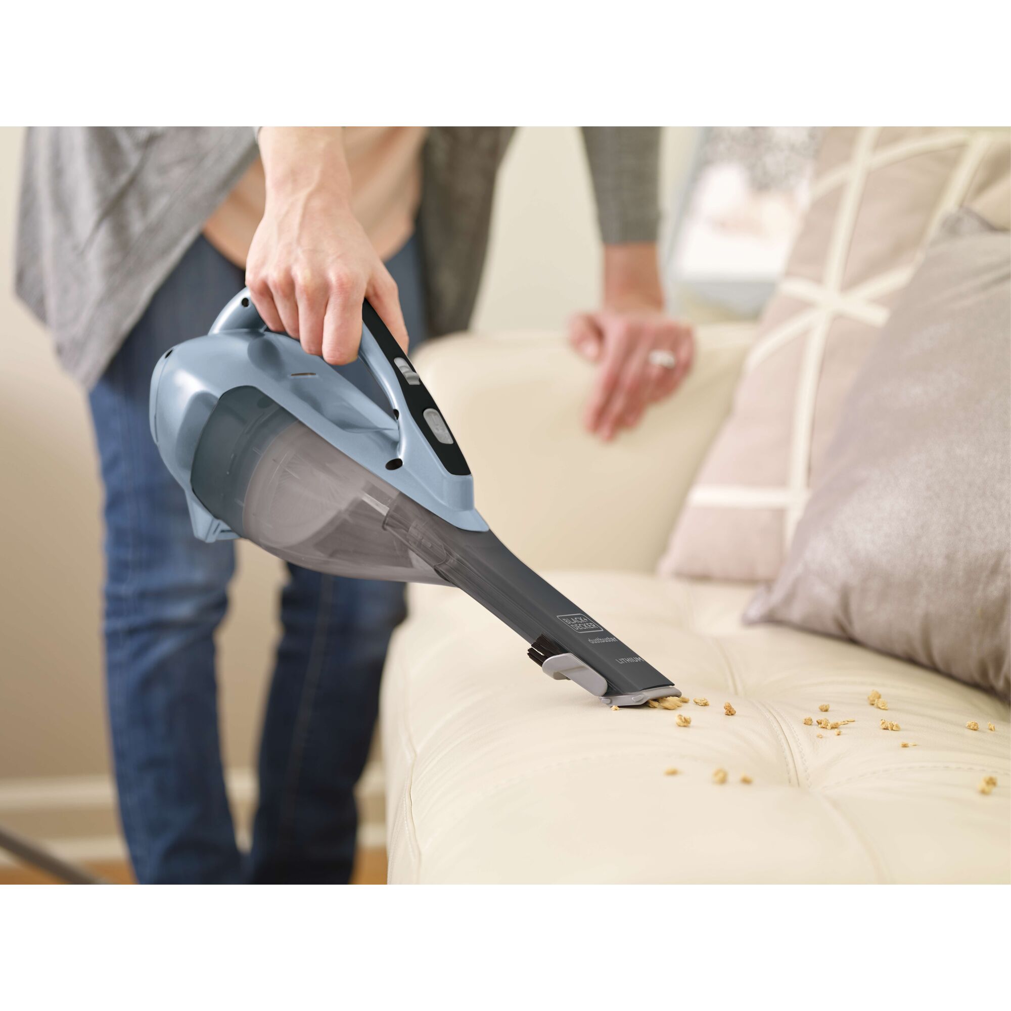 BLACKDECKER HLVA315J32 handheld vacuum cleaning crumbs on a beige sofa in a living room.