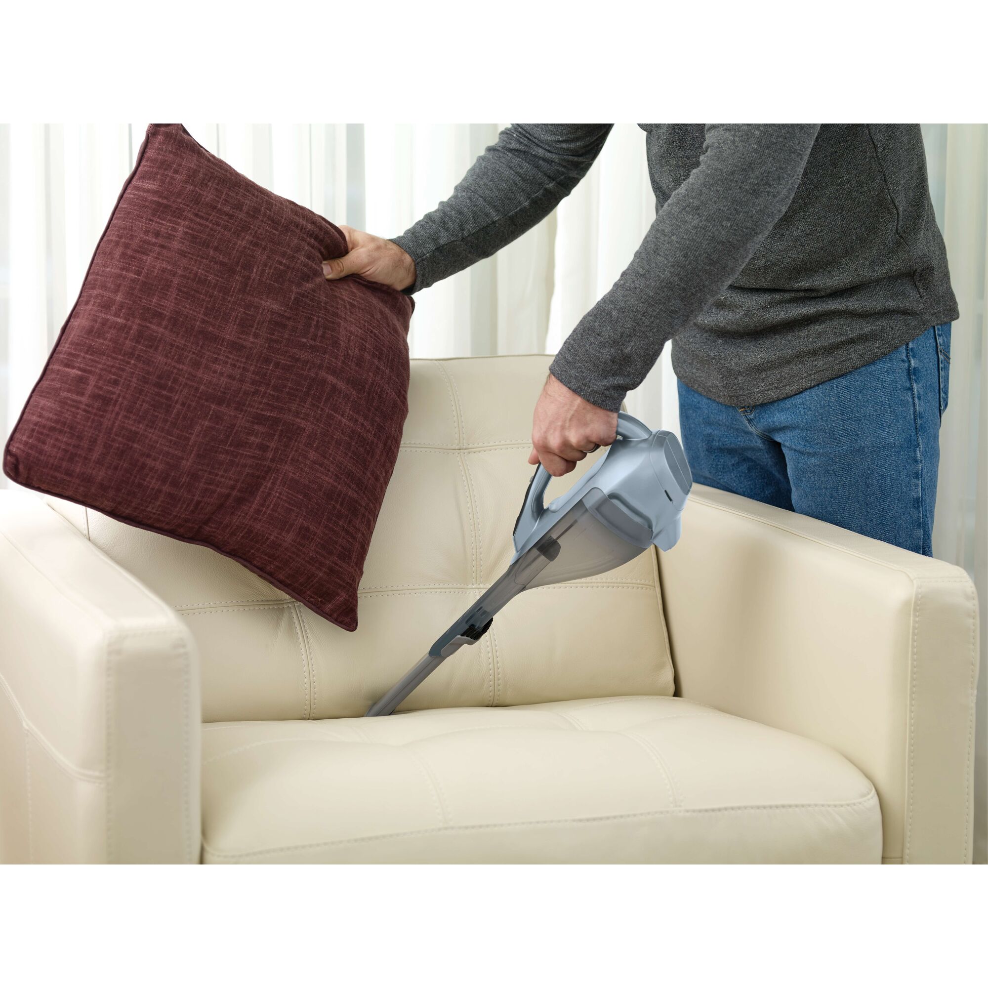 BLACKDECKER HLVA315J32 handheld vacuum cleaning cream armchair under maroon pillow indoor.