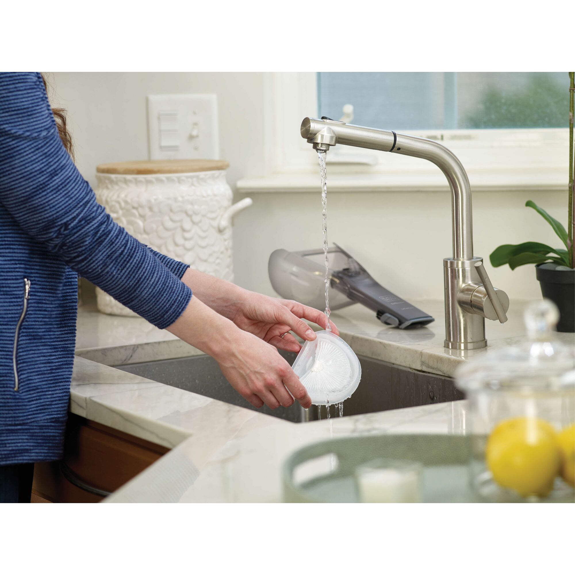 BLACKDECKER HLVA315J32 handheld vacuum on kitchen counter, person rinsing vacuum filter under faucet.