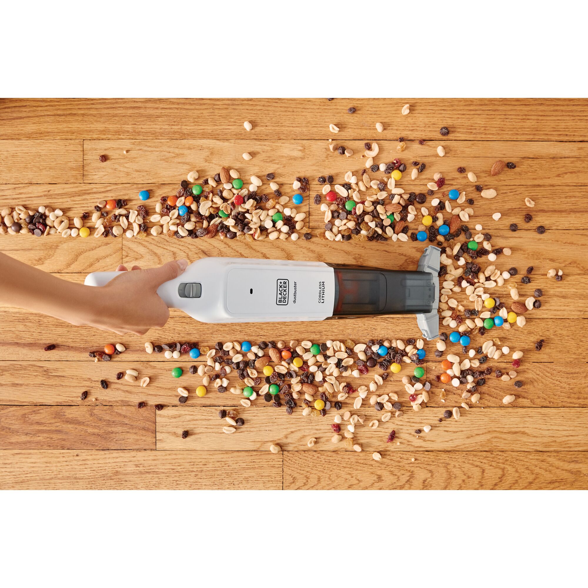BLACK+DECKER HLVC315B handheld vacuum cleaning nuts and candies from wood floor, top view.