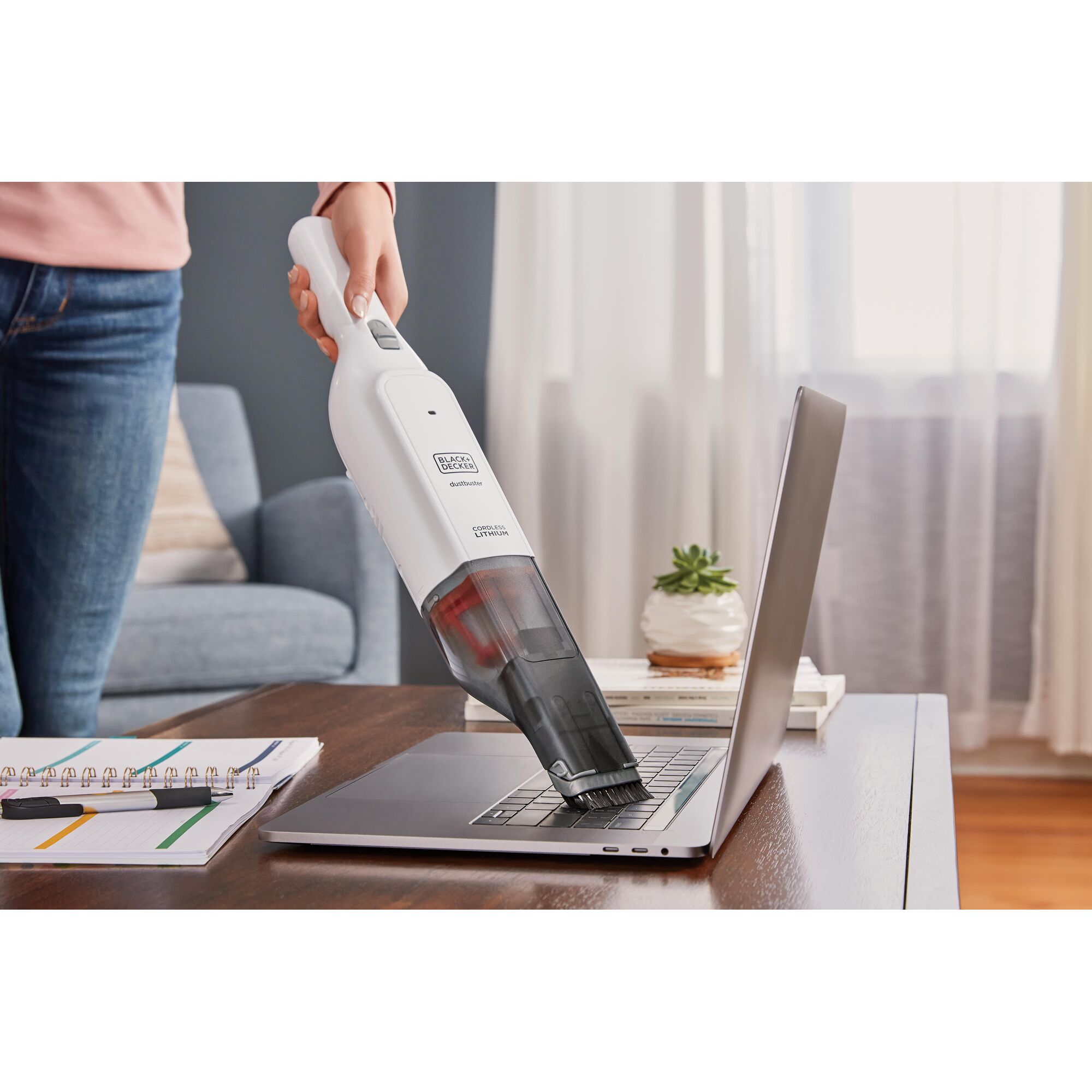 BLACKDECKER HLVC315B handheld vacuum cleaning a laptop keyboard in a modern living room setting.