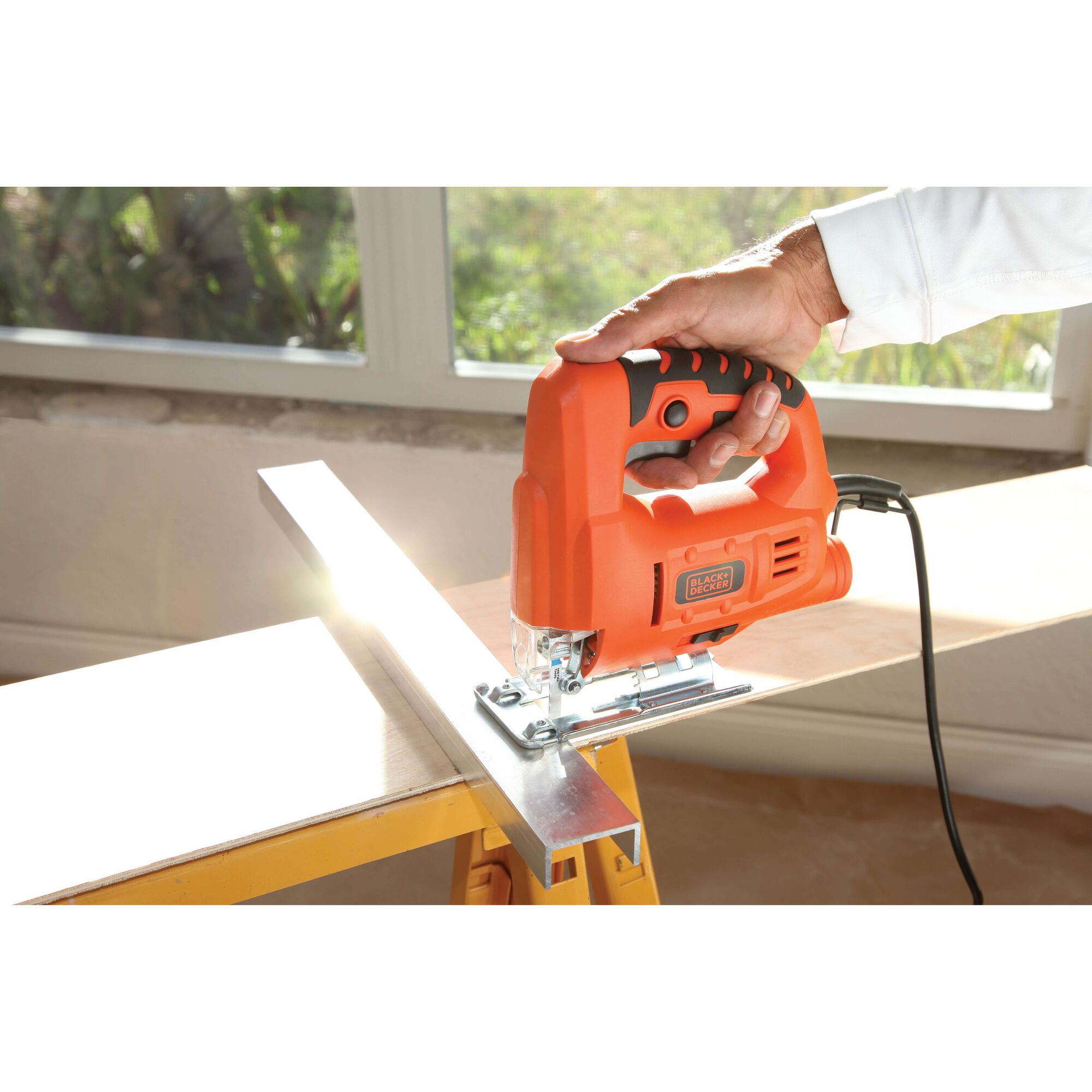 BLACKDECKER JS20 jigsaw in use, orange body, cutting wood with a metal guide, handheld operation.