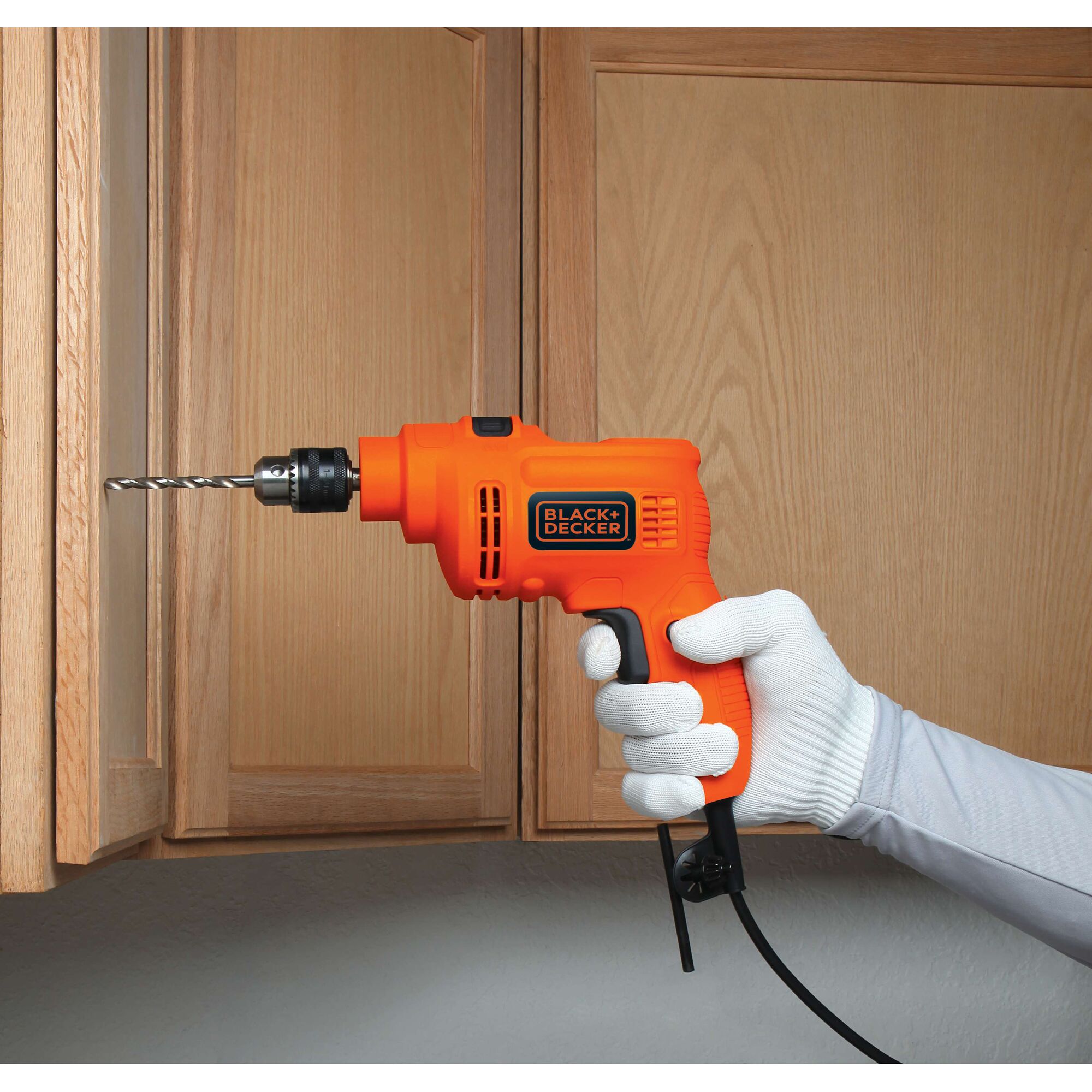 BLACKDECKER KR5010 orange corded drill held by gloved hand drilling into wooden cabinet.