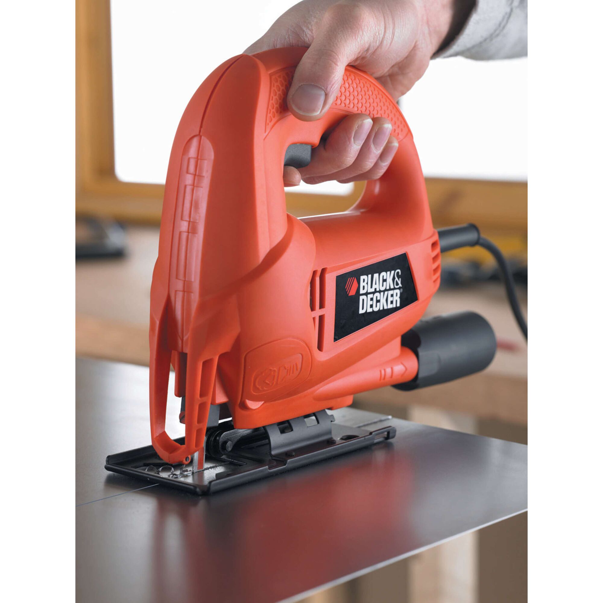 BLACKDECKER KS600E jigsaw power tool cutting metal sheet, close-up with hand holding handle.