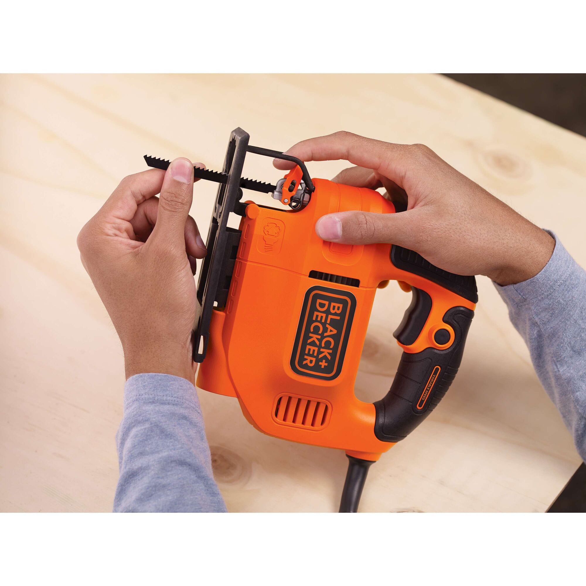 Photo of BLACKDECKER KS701E jigsaw being adjusted, orange and black body held by hands on wooden surface.