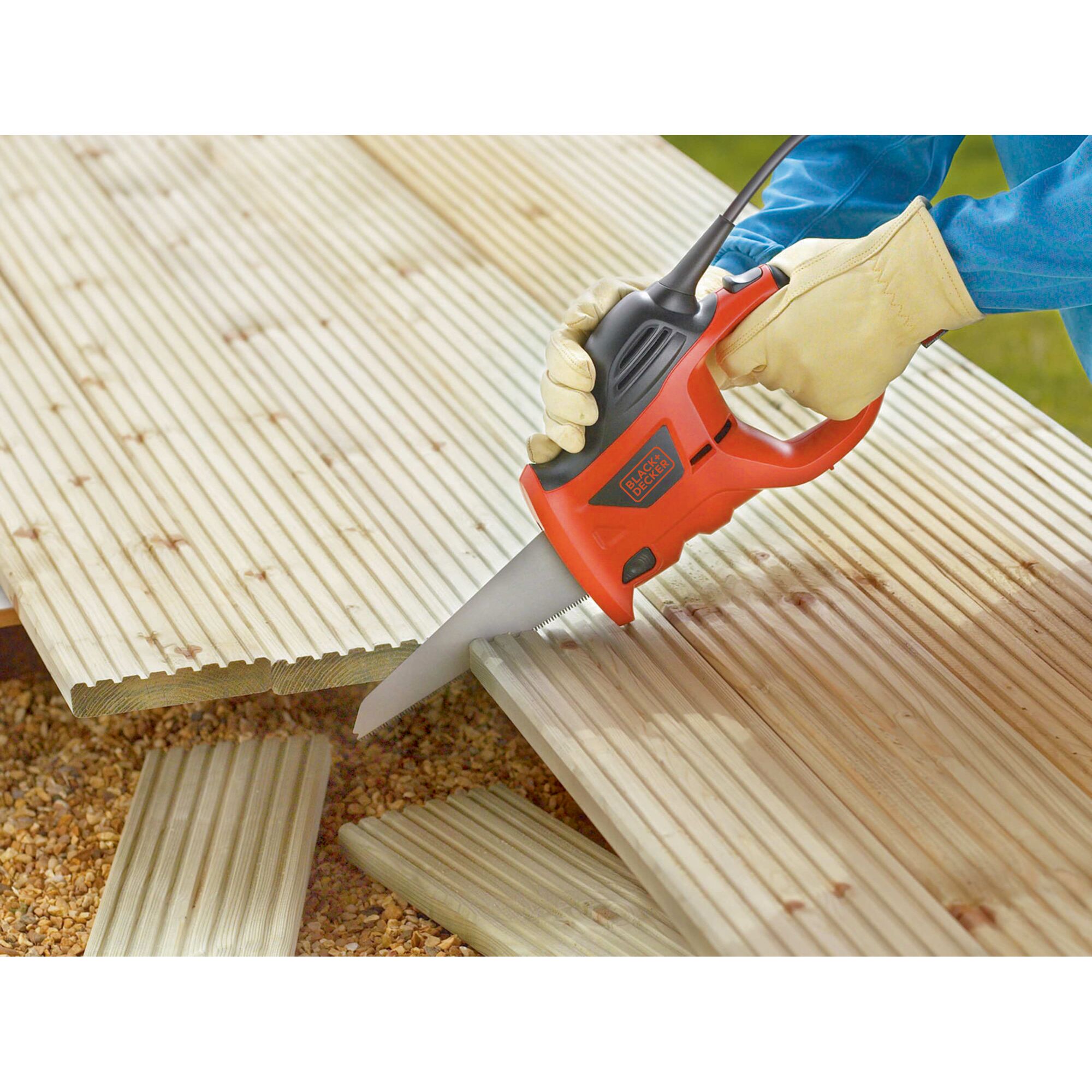 A person wearing gloves is using a BLACK+DECKER electric saw to cut wooden boards placed outdoors.