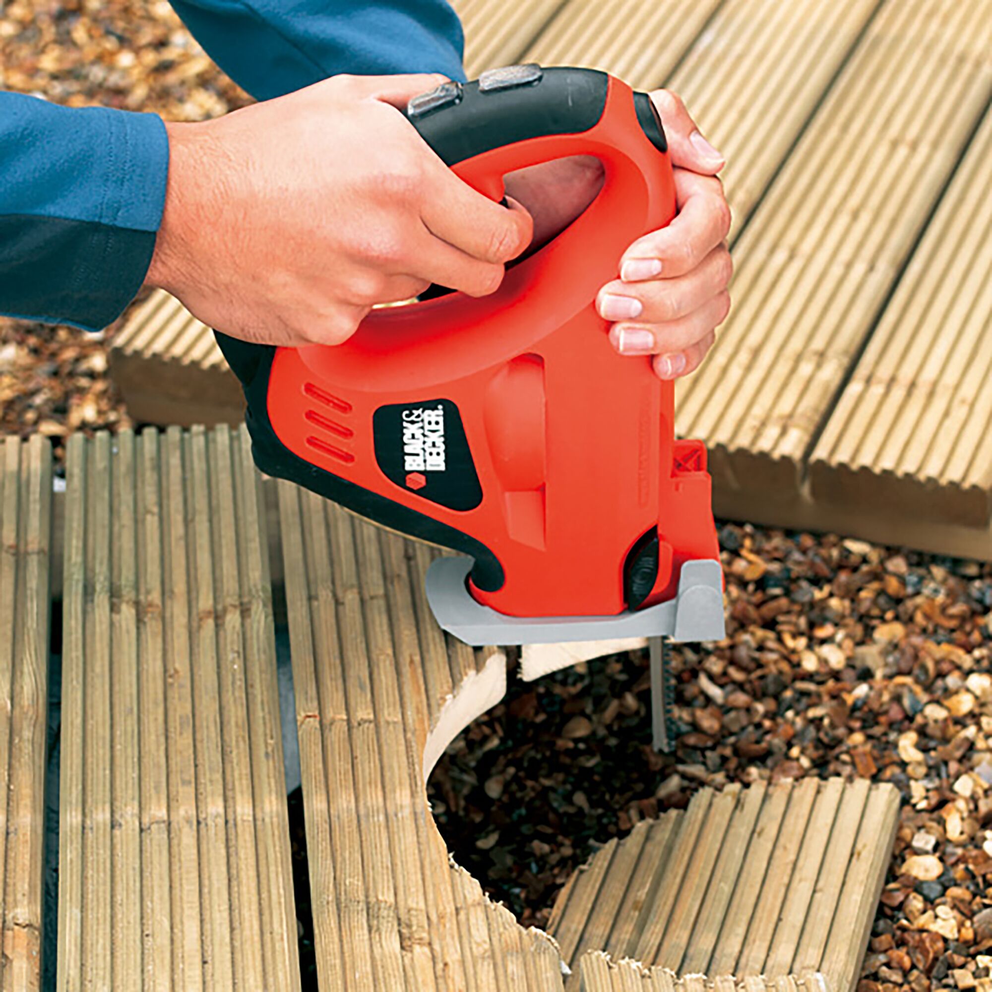 BLACKDECKER KS900G jigsaw cutting curved shapes in wooden decking, close-up in outdoor setting.