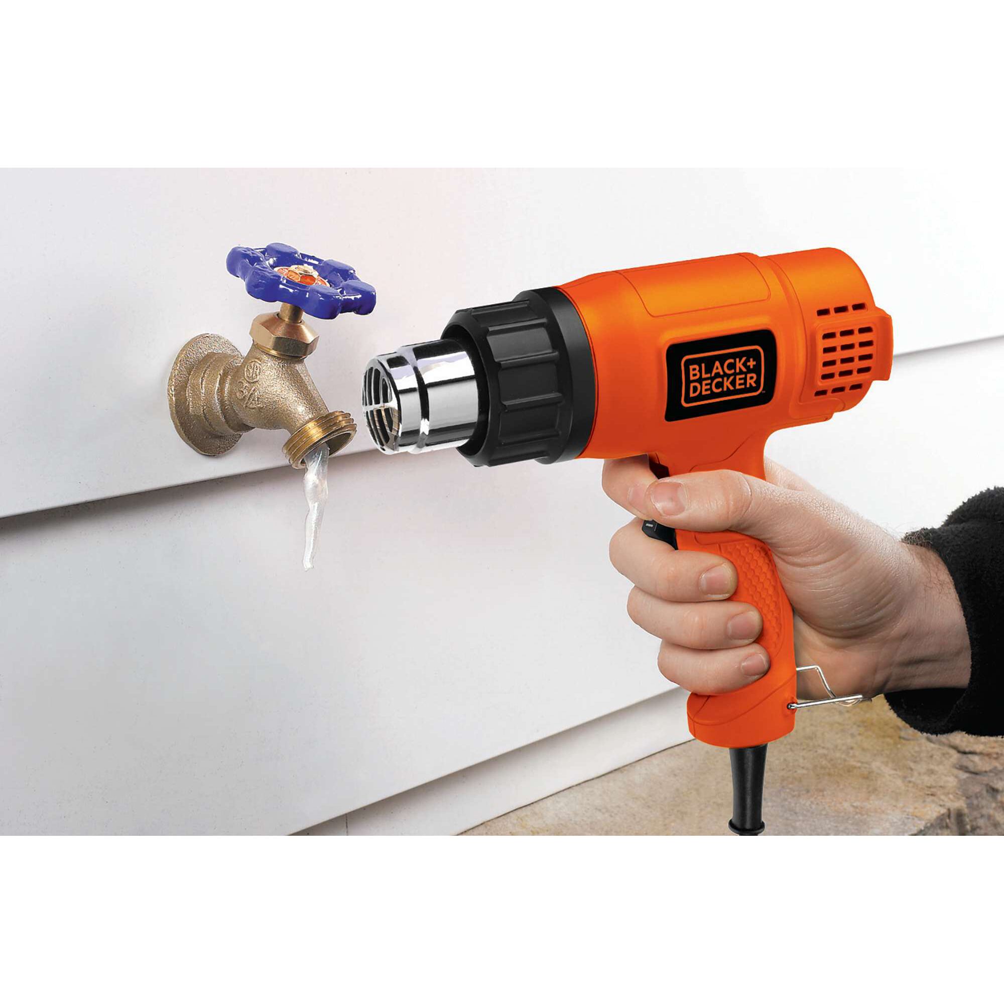 Photo of BLACK+DECKER KX1800 orange heat gun thawing ice on outdoor brass faucet, close-up view.