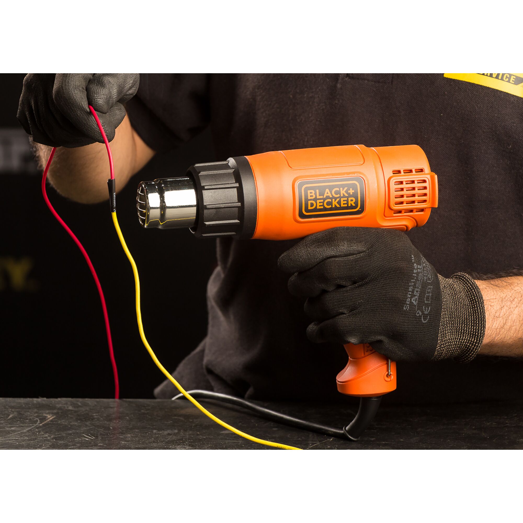 Photo of BLACK+DECKER heat gun KX1800 in use, orange body, heating electrical wires, held by gloved hand.