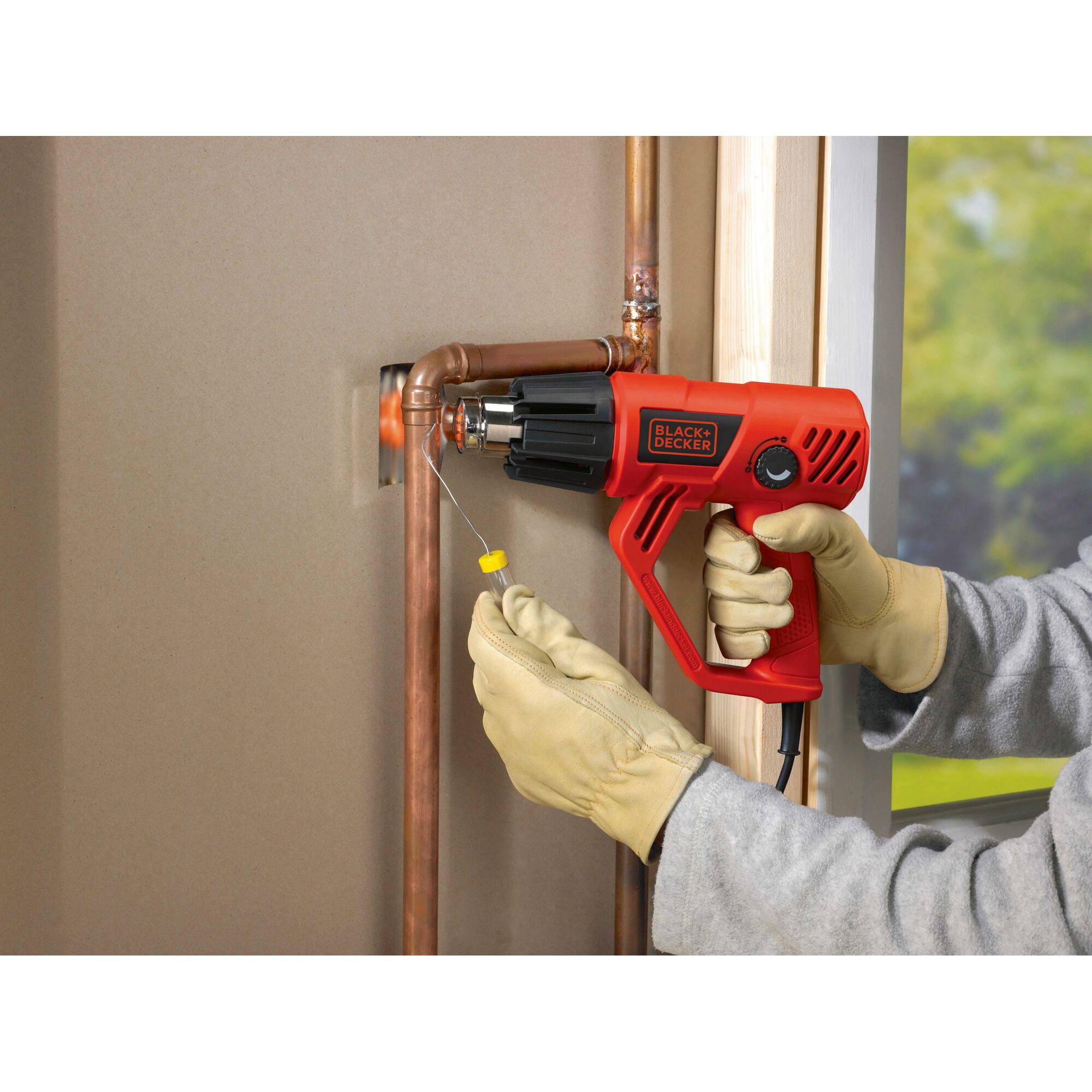 BLACKDECKER KX2001K heat gun used on copper pipes, person wearing gloves, indoor setting.