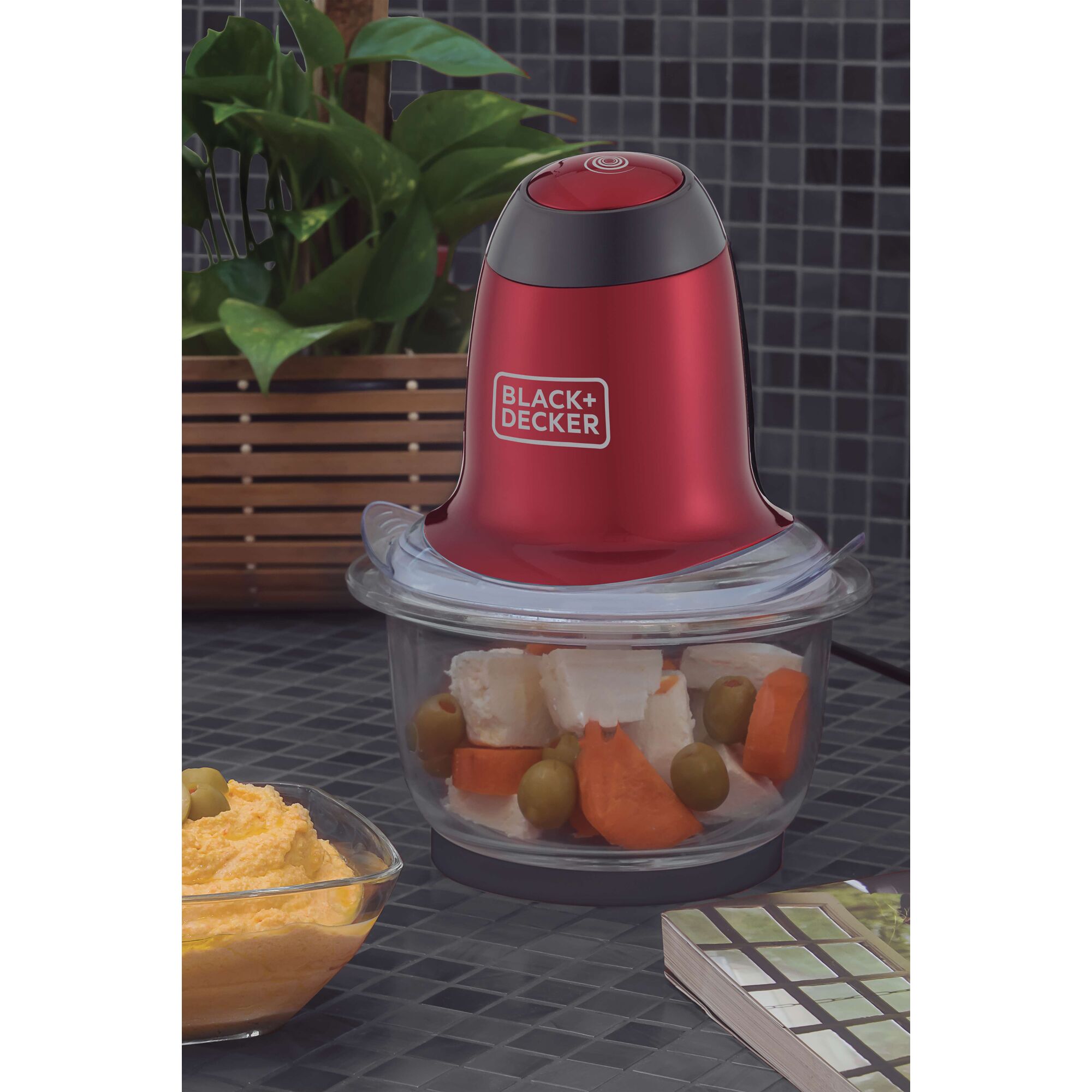BLACK+DECKER MP200V food processor in red and black with glass bowl, filled with vegetables, on a kitchen counter.