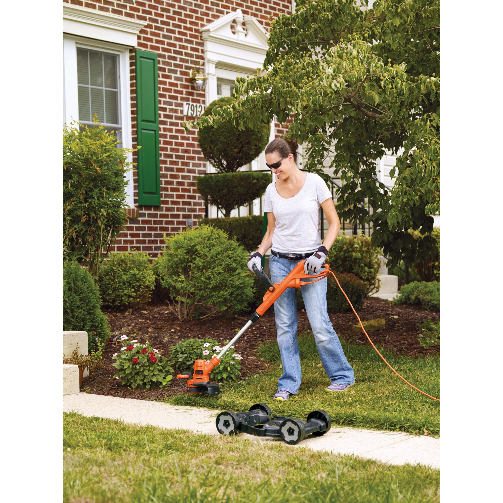 A woman is mowing the garden using a BLACK+DECKER String Trimmer/Edger & Lawn Mower.