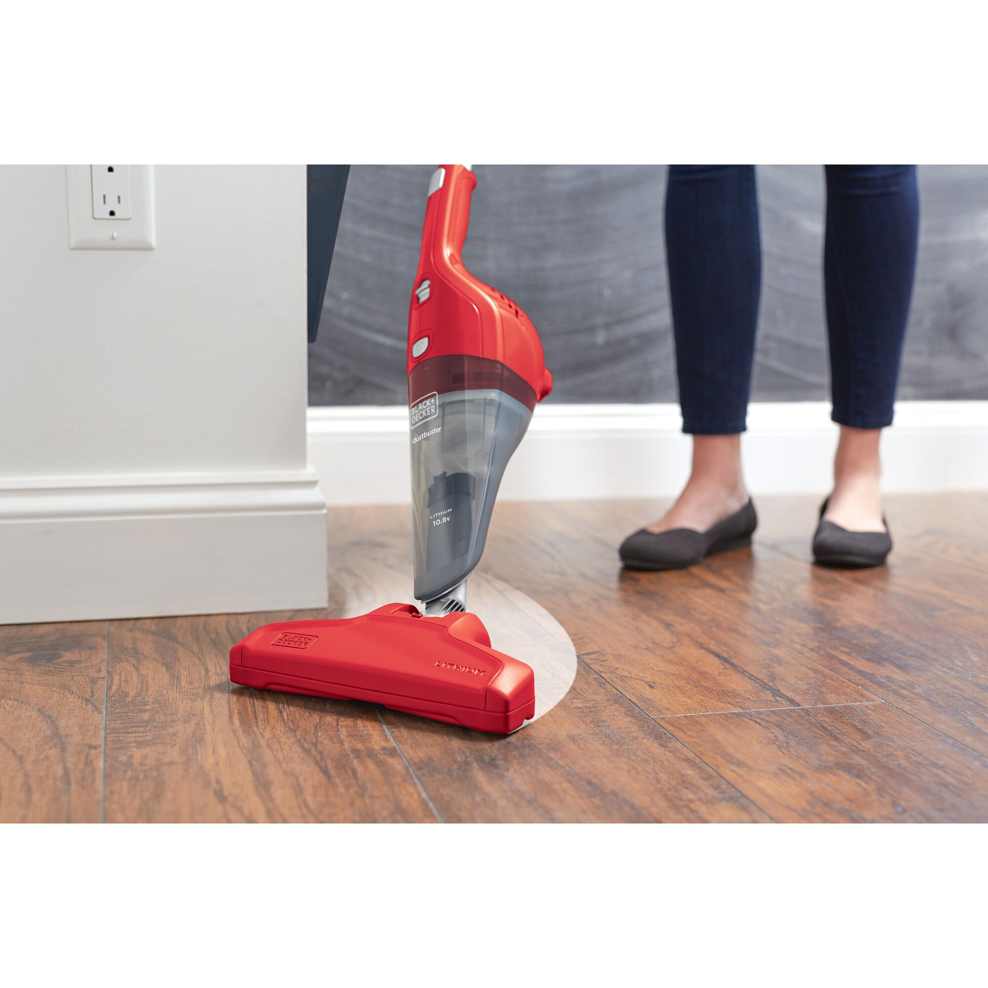 BLACKDECKER NSVA315JR red cordless stick vacuum cleaner on hardwood floor with person standing nearby.