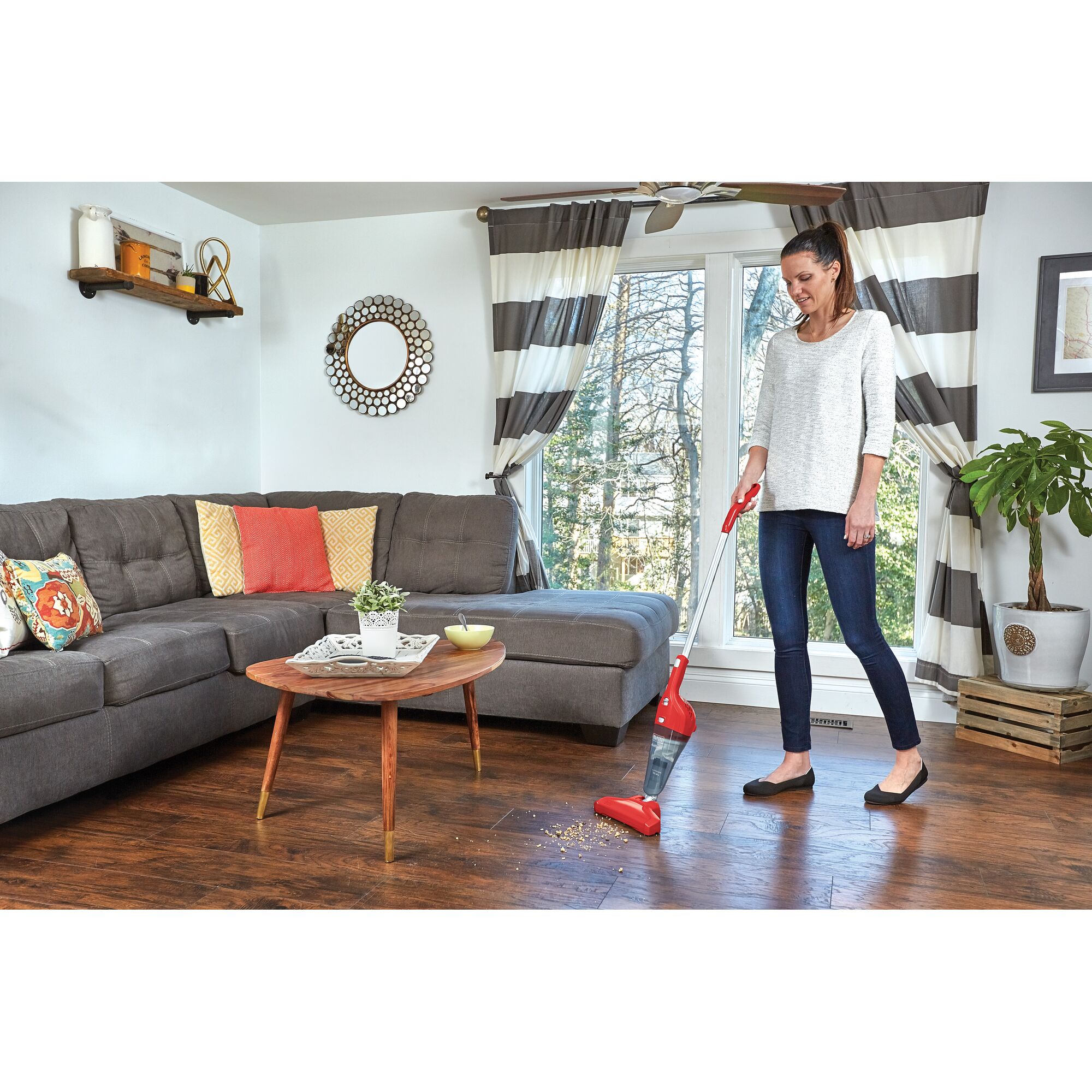 BLACK+DECKER NSVA315JR stick vacuum cleaning crumbs on hardwood living room floor near gray sofa.
